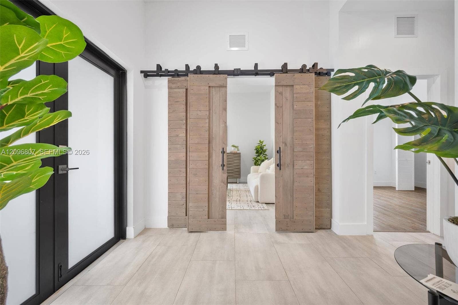 Double sliding barn doors with a matte black metal track system, wood-finish flooring, and black-framed glass entry door