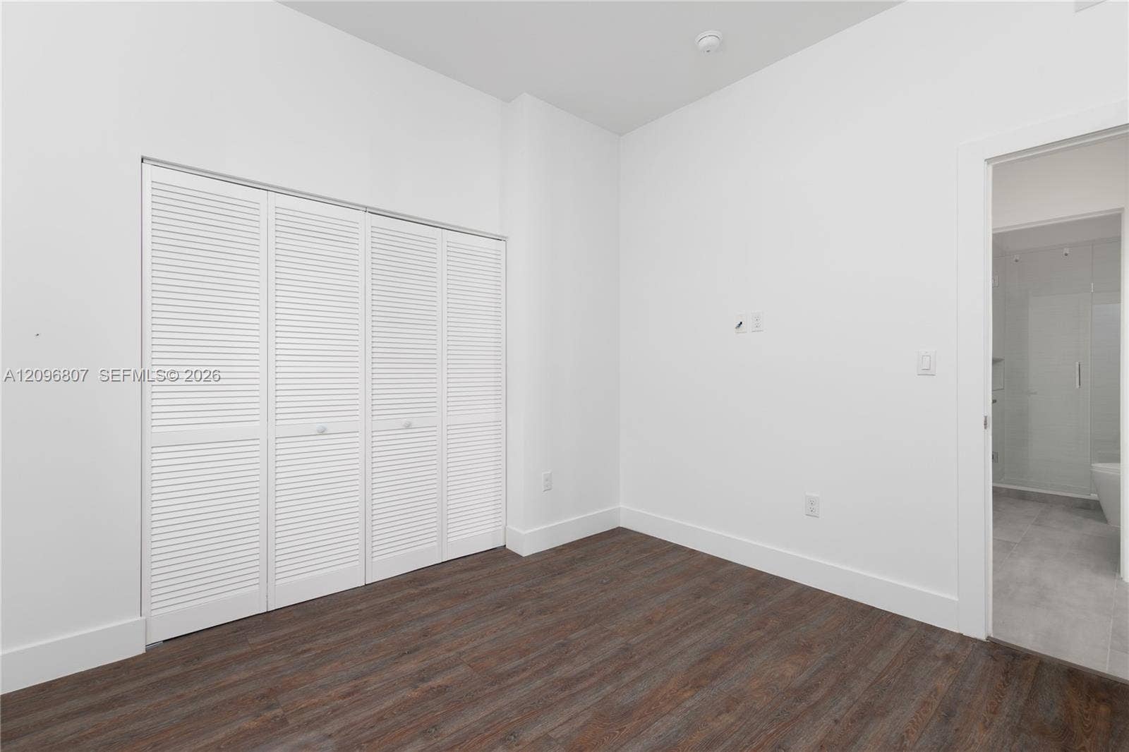 Room featuring wood-finish flooring, white walls, and a four-panel louvered closet door