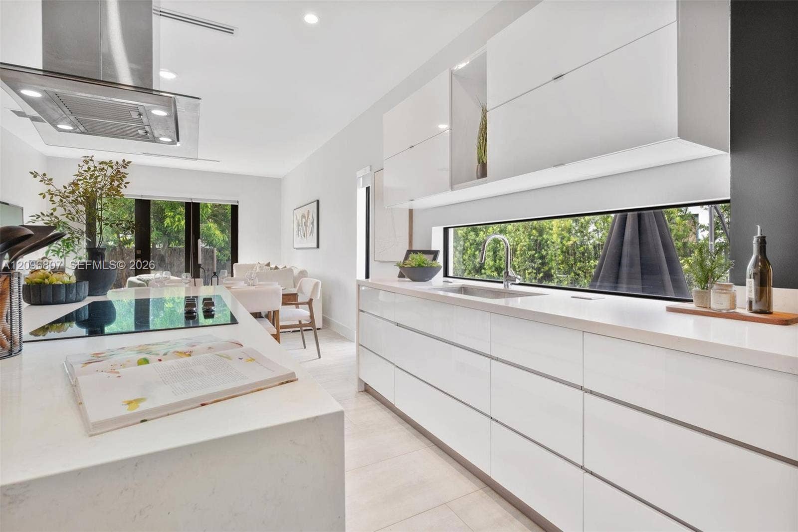 Contemporary kitchen featuring flat-panel high-gloss cabinetry, stone-surface countertops, a full-width horizontal backsplash window, a stainless steel undermount sink, and a stainless steel ceiling-mounted range hood