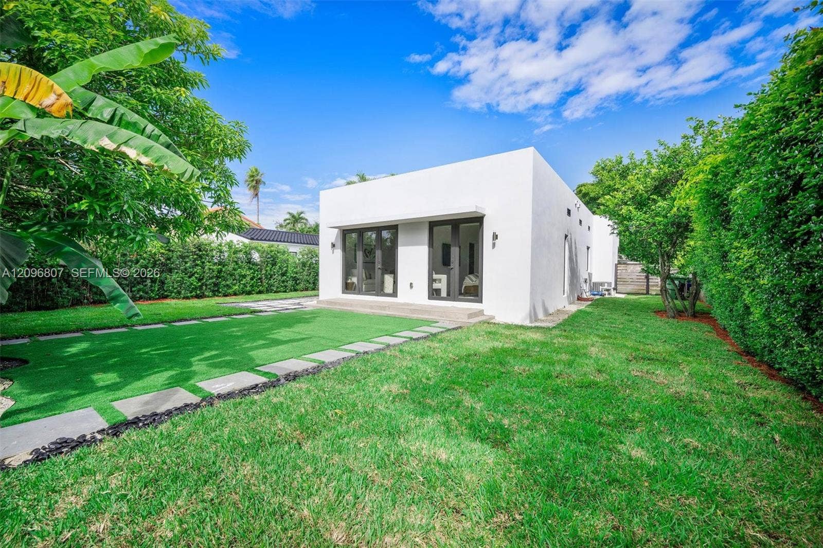 Minimalist exterior with smooth white stucco, dual sets of glass-paneled double doors, manicured turf lawn, and custom stone paver walkway