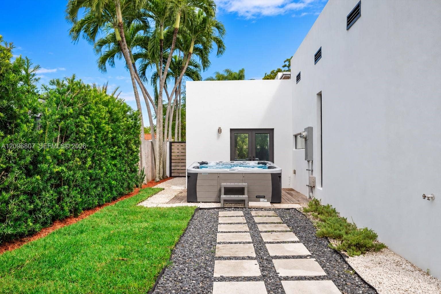 Outdoor space featuring a standalone spa, stone paver walkway with gravel surround, manicured lawn, and mature palm trees