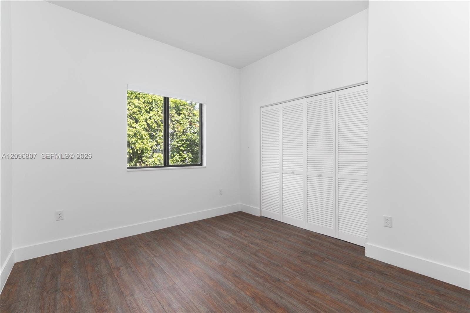 Interior room featuring wood-finish flooring, white walls, and a window with black trim