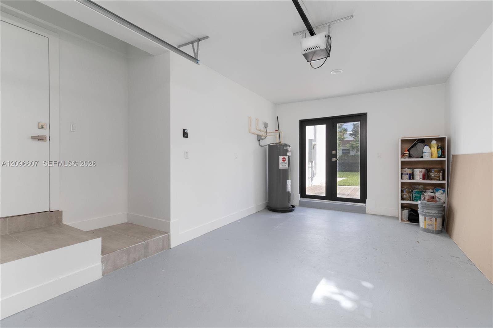 Garage interior featuring painted concrete flooring, a tiled step entry, and a double-glass door