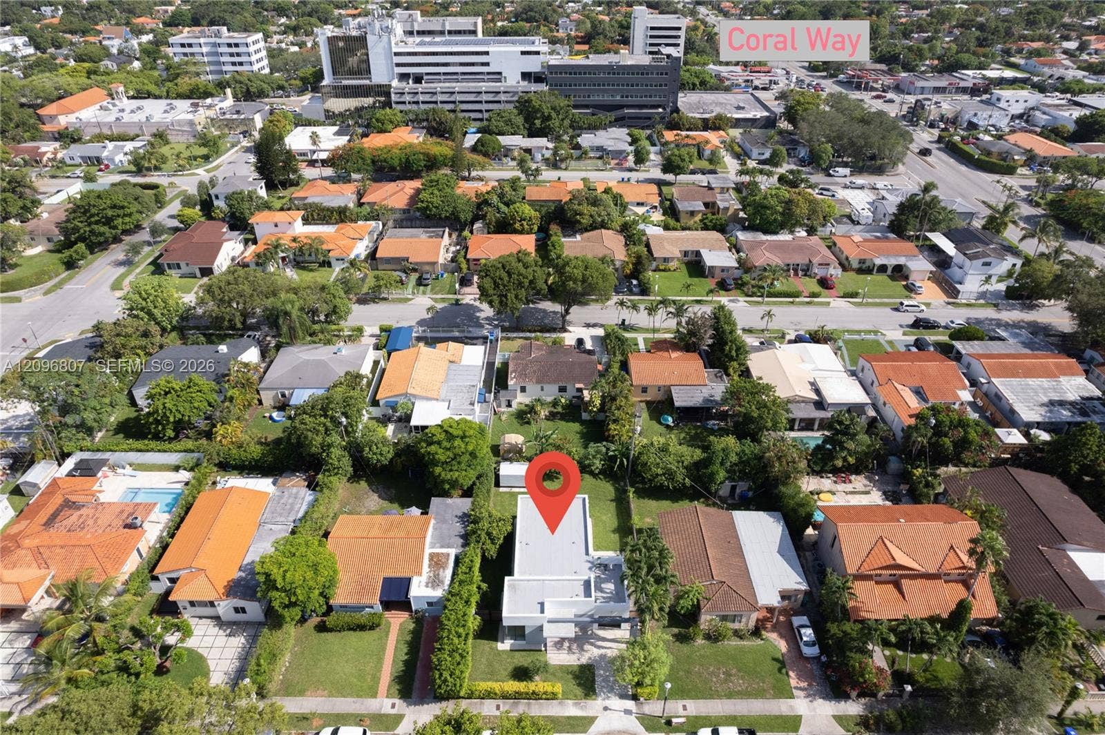 Aerial perspective of residential property featuring a flat roof structure, grass lawn, and dense perimeter landscaping