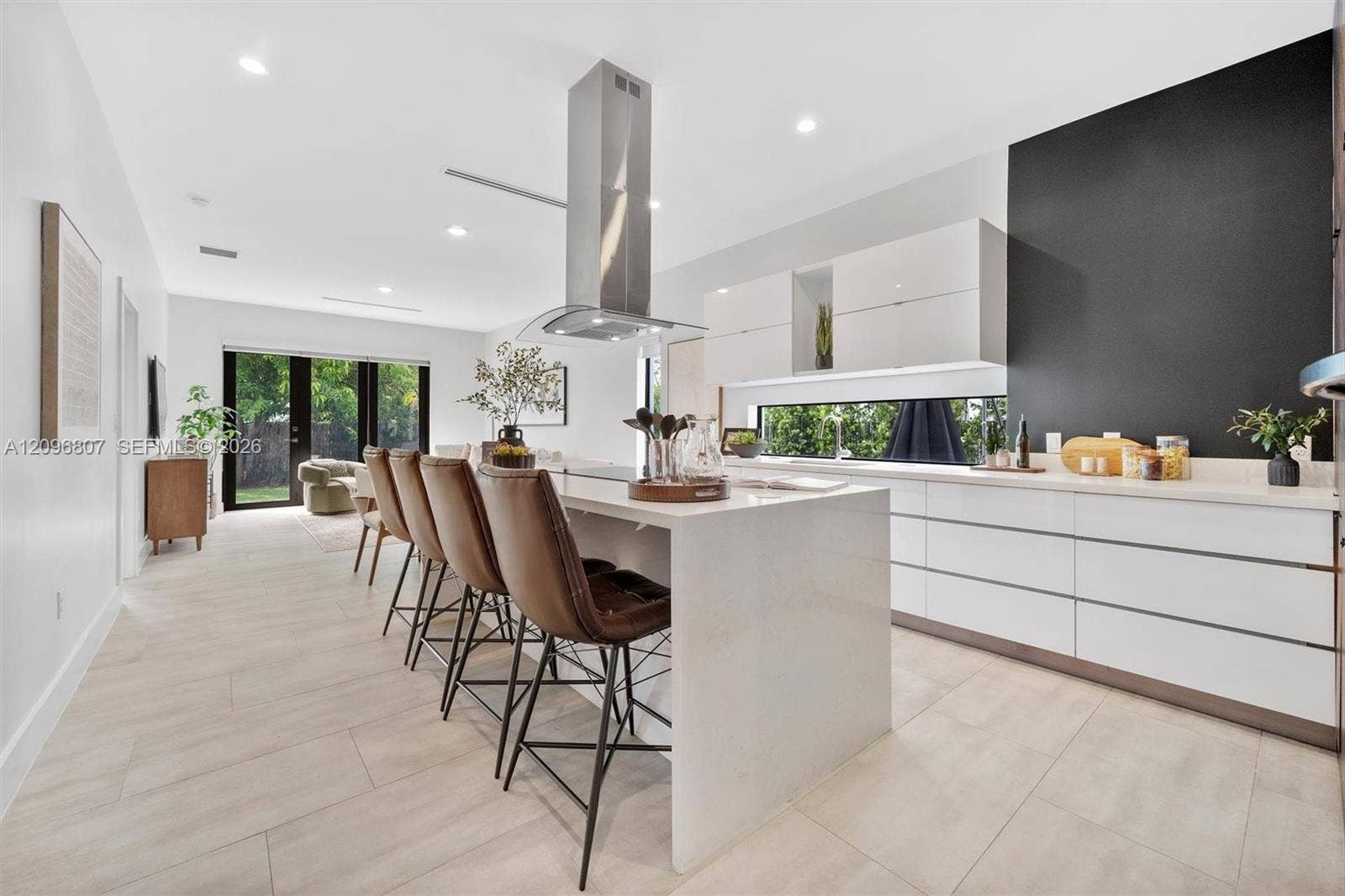 Kitchen featuring a large central island with quartz countertops, minimalist high-gloss white cabinetry, a stainless steel chimney-style range hood, and porcelain tile flooring