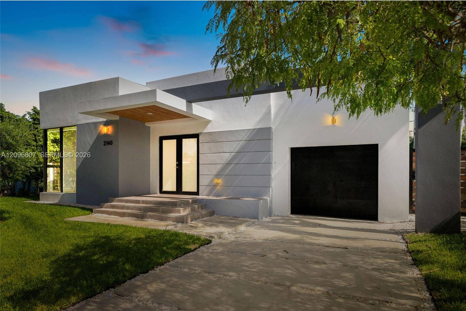 Modern exterior featuring a smooth stucco facade, dual-tone architectural detailing, a covered entrance with wood-paneled ceiling, and a concrete driveway