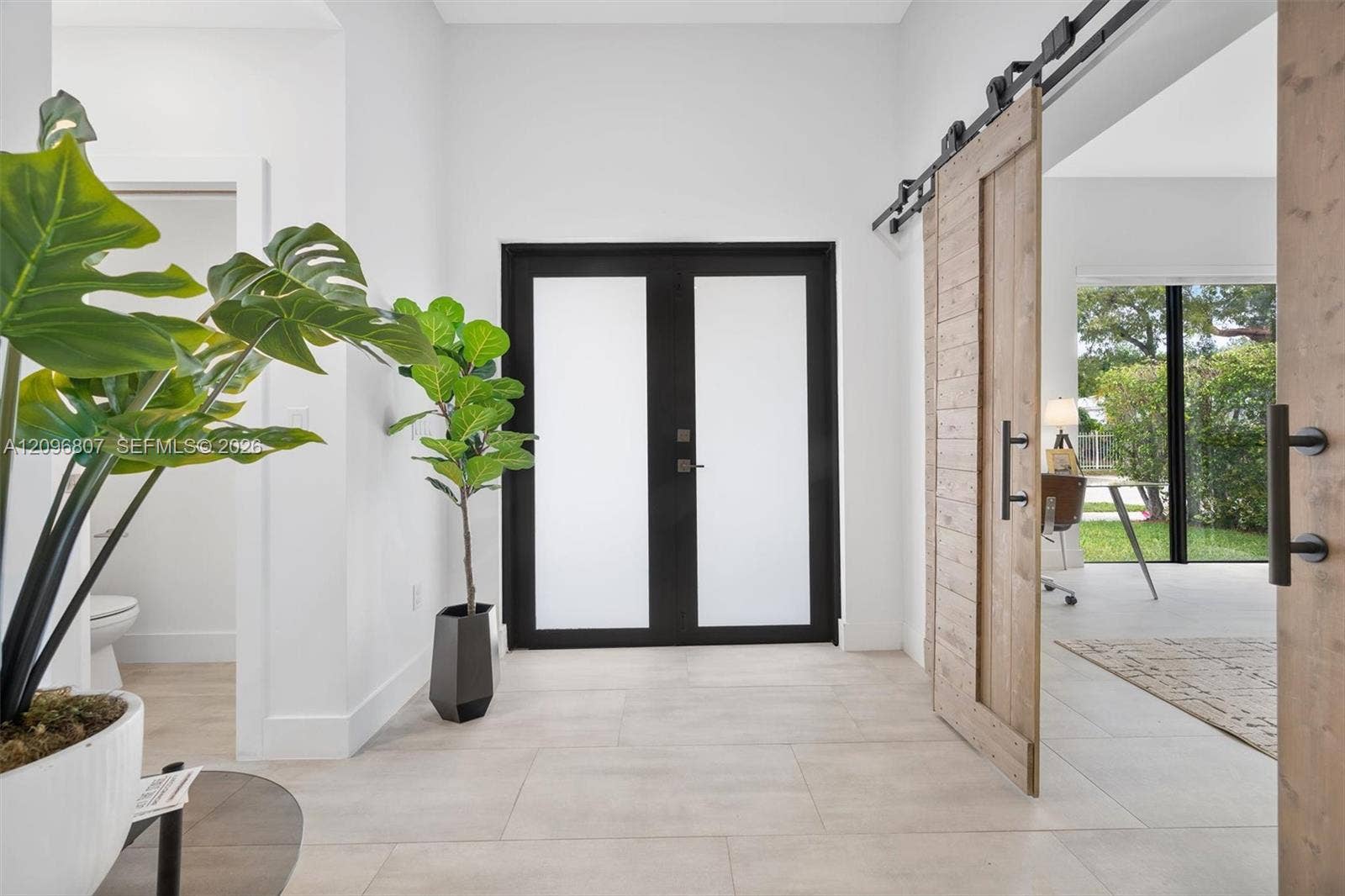 Entryway featuring double doors with frosted glass insets, large-format tile flooring, and wood-finish sliding barn doors with black metal hardware