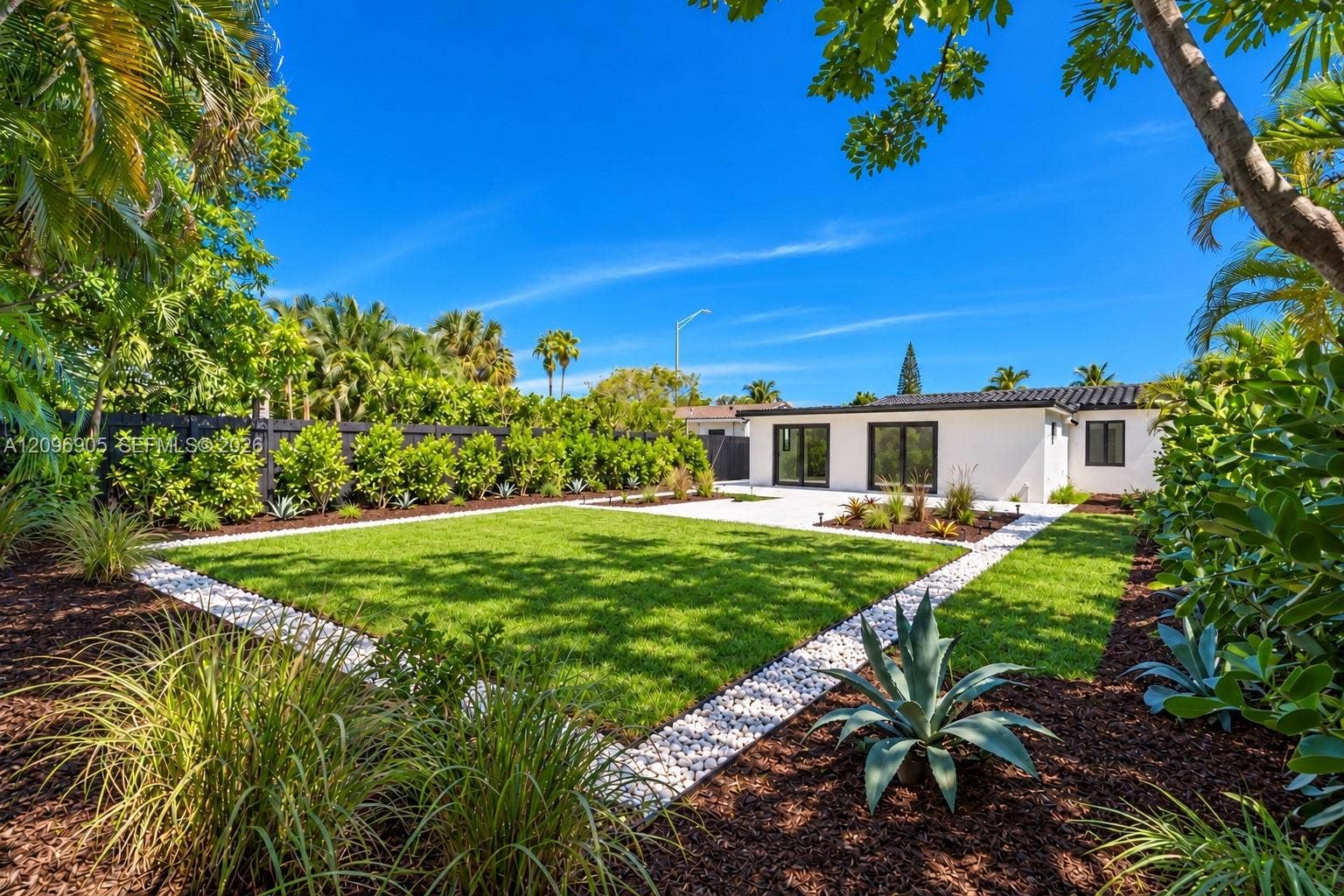 Contemporary white exterior, dark tile roof, multiple large glass doors, expansive green lawn, and mature landscaping
