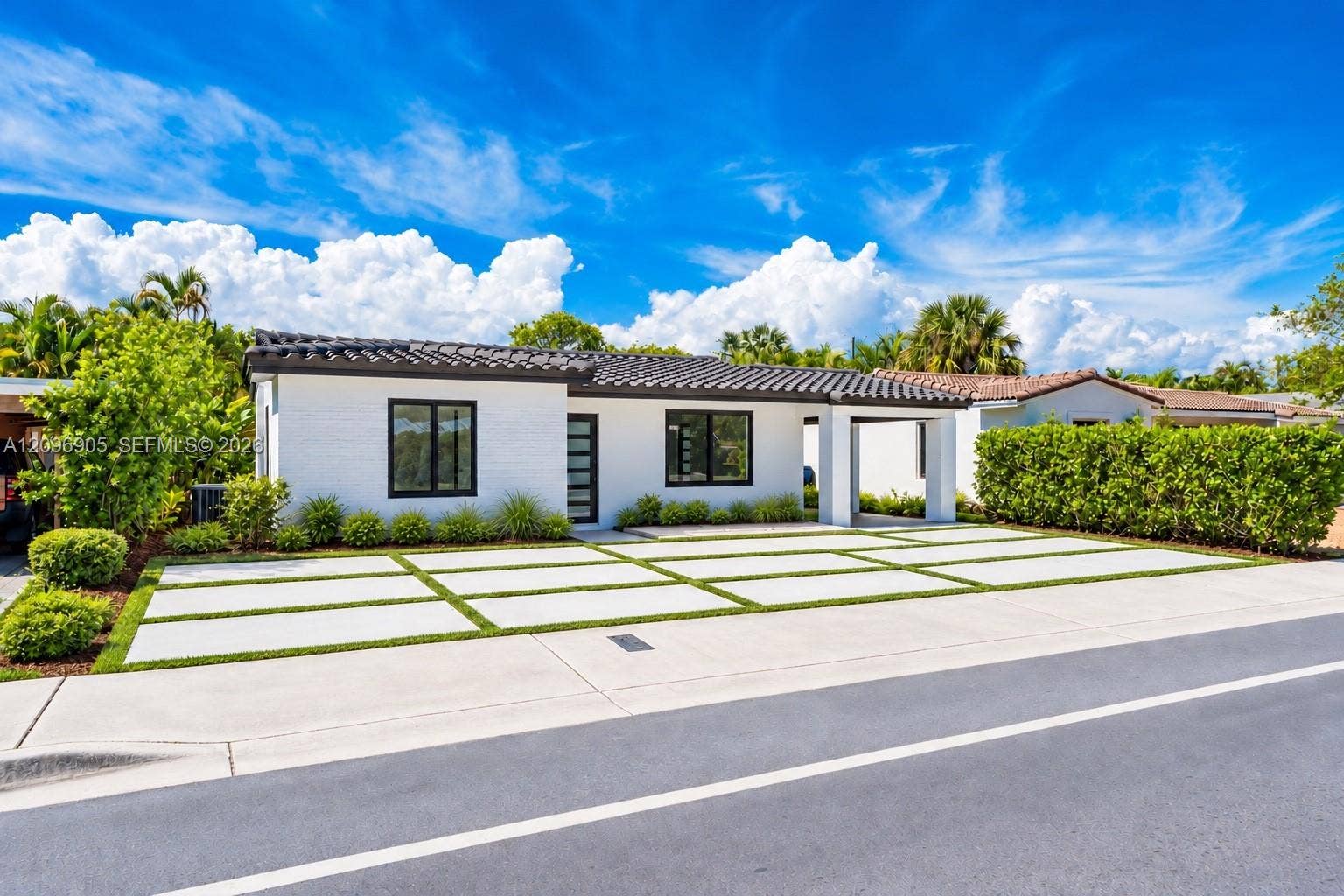 White exterior with black-framed windows, modern driveway with turf accents, black tile roof, and manicured landscaping