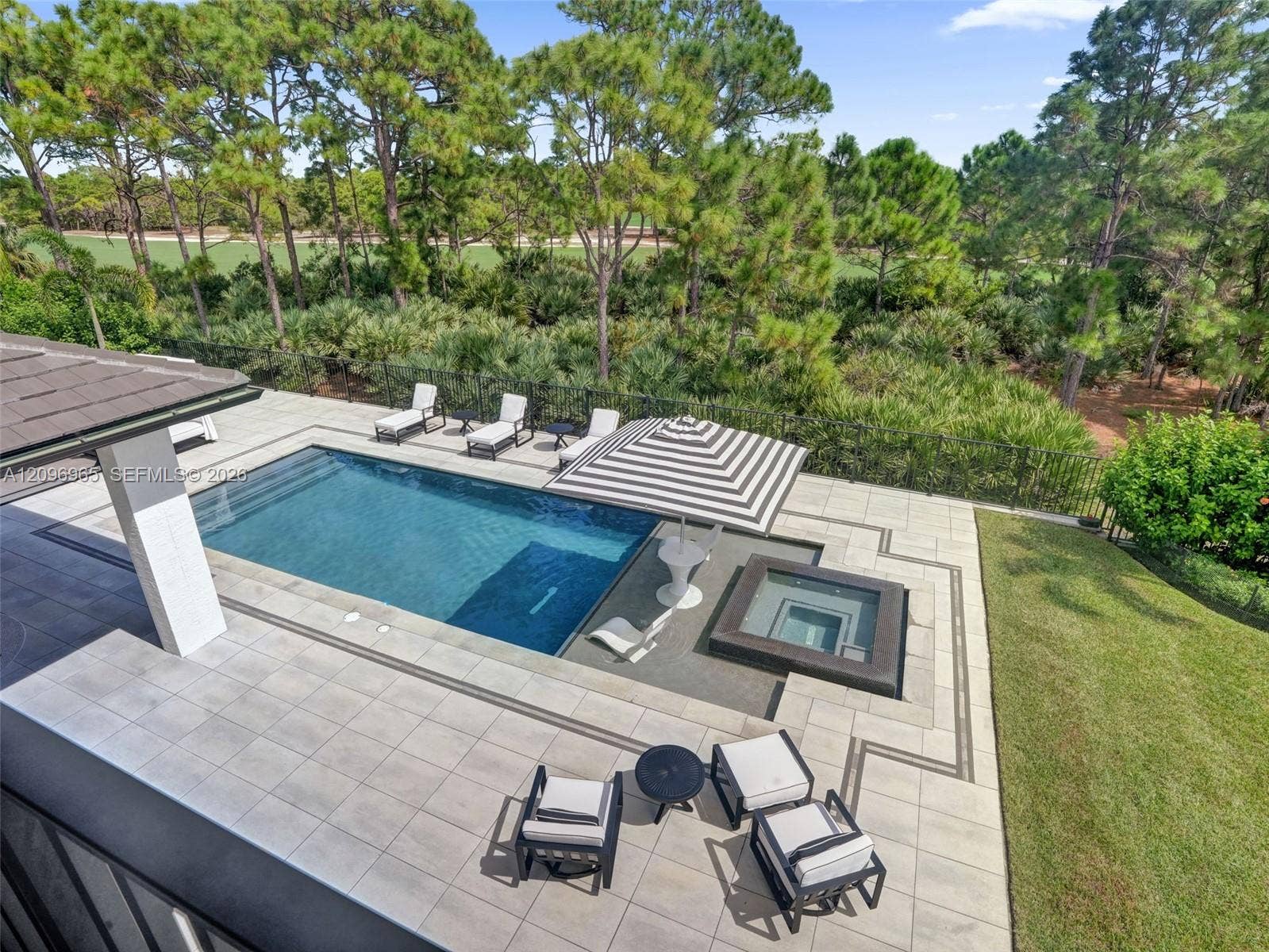 10157 SE Sandpine Lane, Hobe Sound, FL 33455 Outdoor living area featuring a custom pool with an integrated spa, tiled patio, and metal perimeter fencing overlooking a wooded landscape