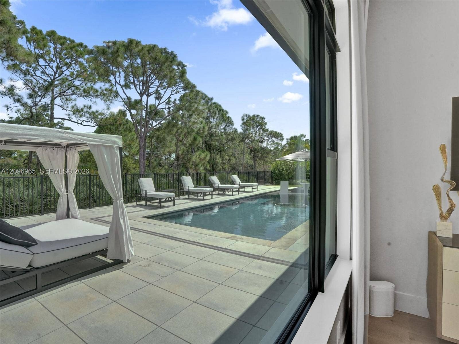 10157 SE Sandpine Lane, Hobe Sound, FL 33455 Outdoor patio with large-format tile flooring, rectangular in-ground pool, metal perimeter fencing, and mature pine trees