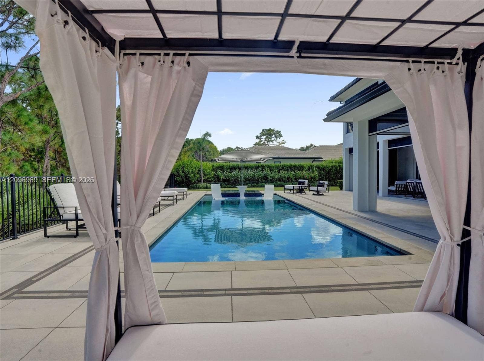 10157 SE Sandpine Lane, Hobe Sound, FL 33455 Rectangular swimming pool featuring a Baja shelf, paved stone deck, metal perimeter fencing, and a built-in covered cabana structure