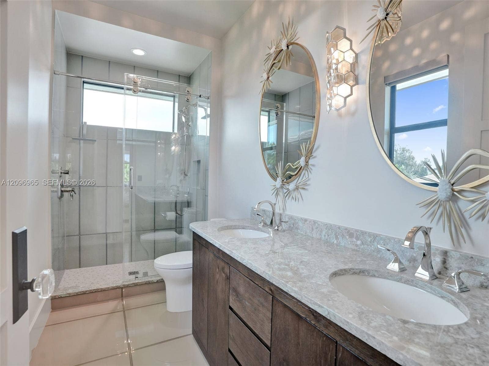 10157 SE Sandpine Lane, Hobe Sound, FL 33455 Dual-sink vanity with stone-finish countertop and wood-finish cabinetry, paired with a glass-enclosed shower featuring tile surrounds and wall-mounted plumbing fixtures