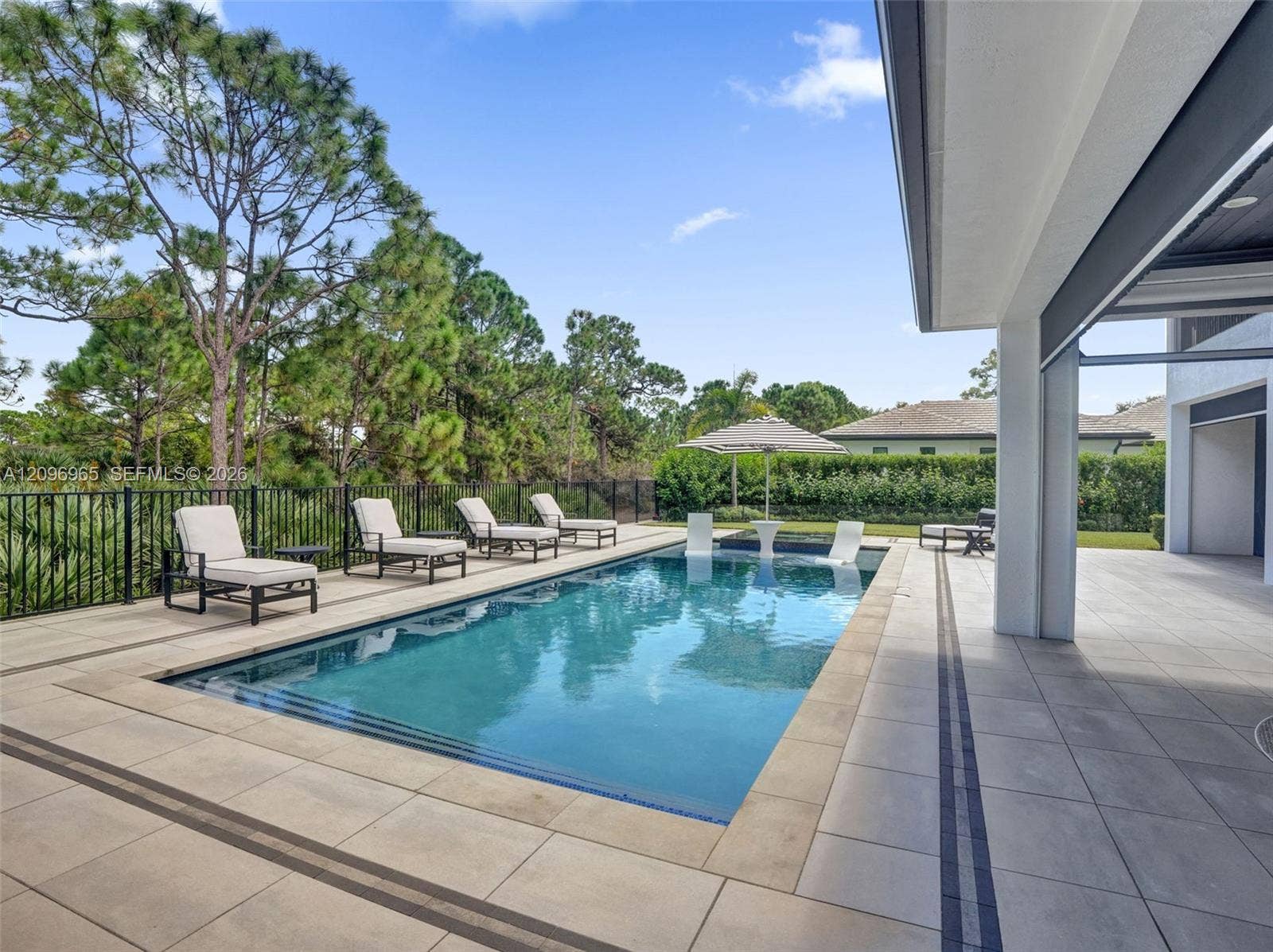 10157 SE Sandpine Lane, Hobe Sound, FL 33455 Rectangular swimming pool featuring a tanning ledge, travertine-style tiled deck, and black metal perimeter fencing