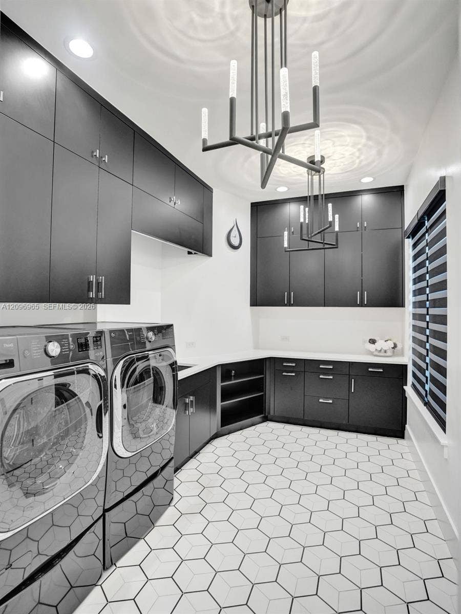 10157 SE Sandpine Lane, Hobe Sound, FL 33455 Laundry room featuring dark cabinetry with brushed metal hardware, white stone countertops, geometric floor tile, and modern linear pendant lighting