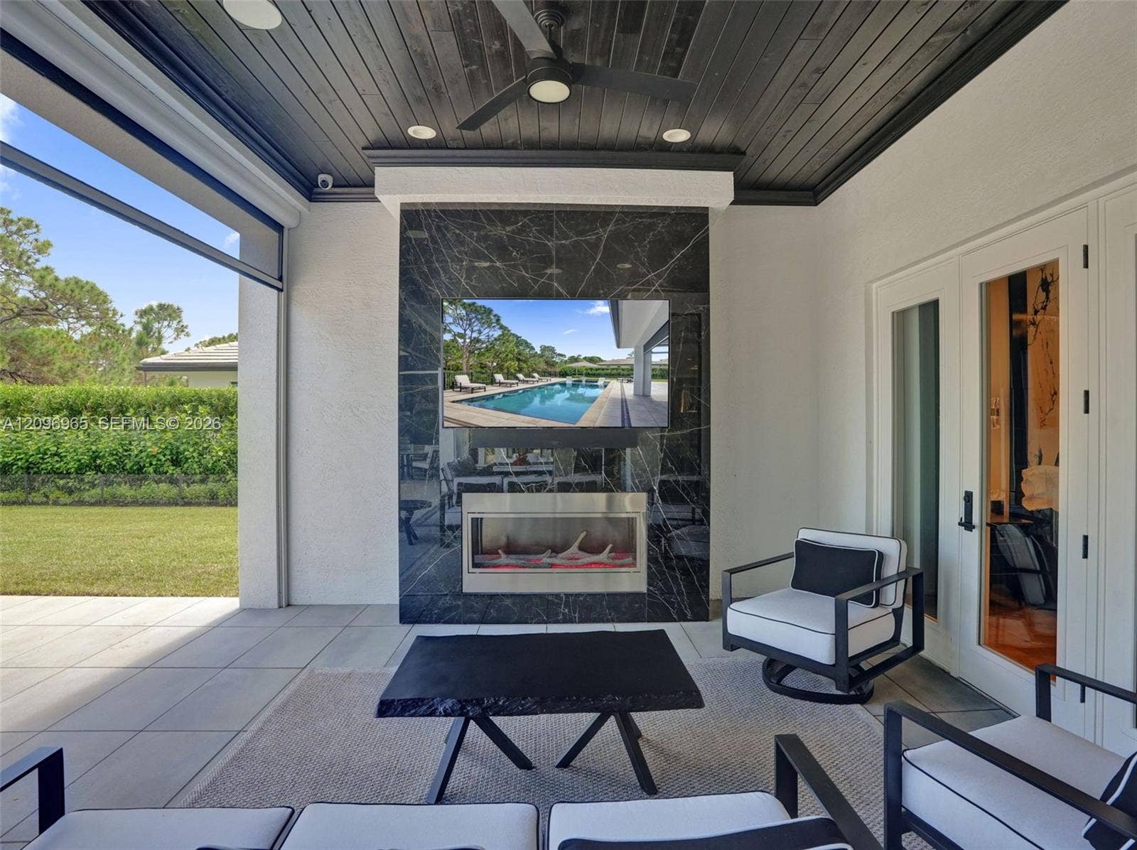 10157 SE Sandpine Lane, Hobe Sound, FL 33455 Covered lanai featuring a black shiplap ceiling, recessed lighting, ceiling fan, and a floor-to-ceiling stone fireplace surround with integrated stainless steel firebox