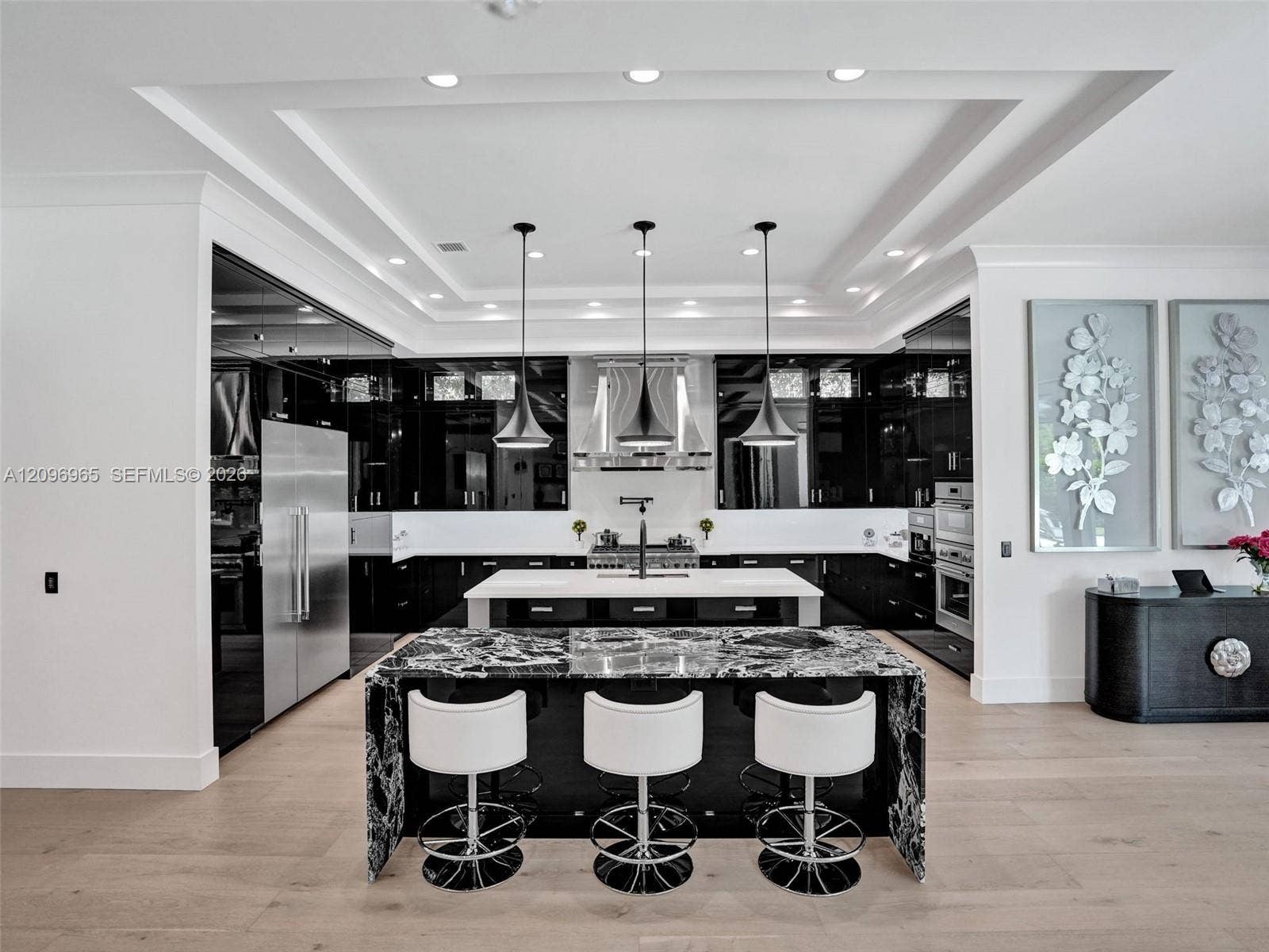 10157 SE Sandpine Lane, Hobe Sound, FL 33455 Kitchen featuring high-gloss cabinetry, stone-surface waterfall island with seating, wood-finish flooring, stainless steel appliances, and a recessed tray ceiling with pendant lighting