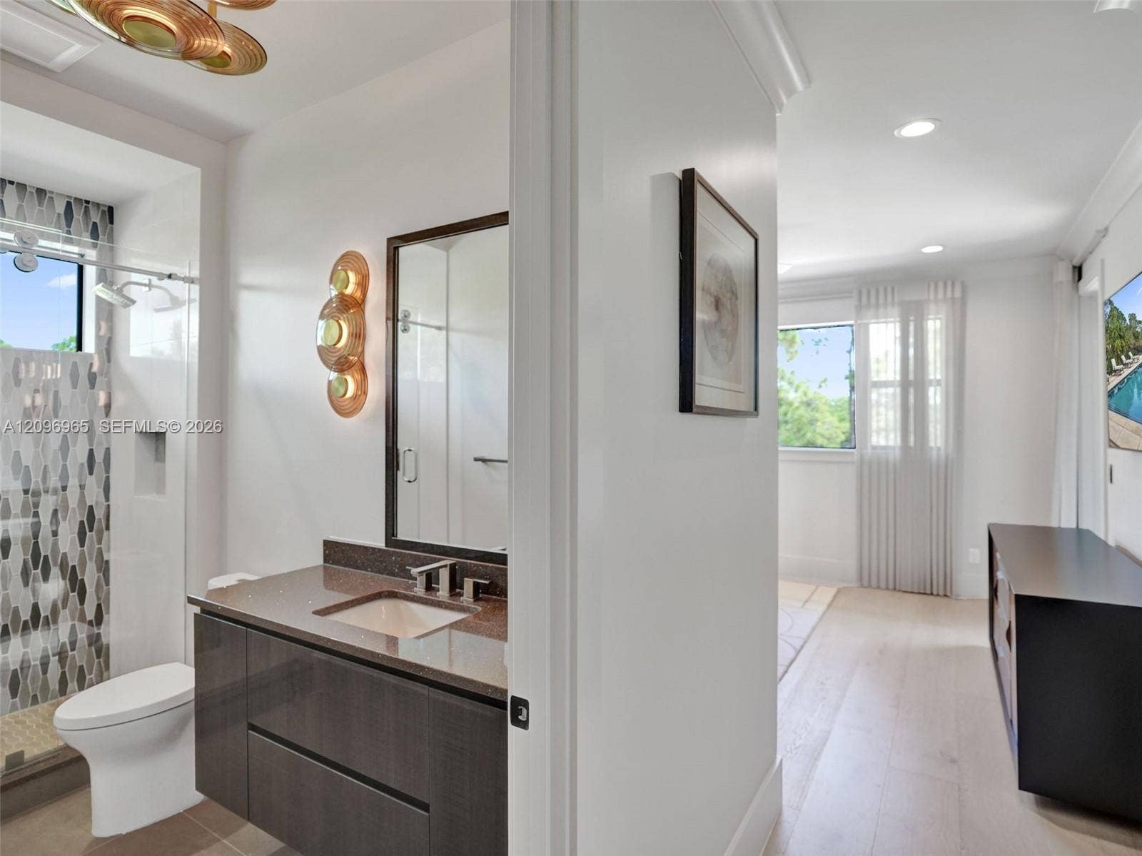 10157 SE Sandpine Lane, Hobe Sound, FL 33455 Bathroom featuring a dark-finish floating vanity with a solid-surface countertop, an undermount sink, patterned wall tile within the glass-enclosed shower, and decorative metallic wall sconces