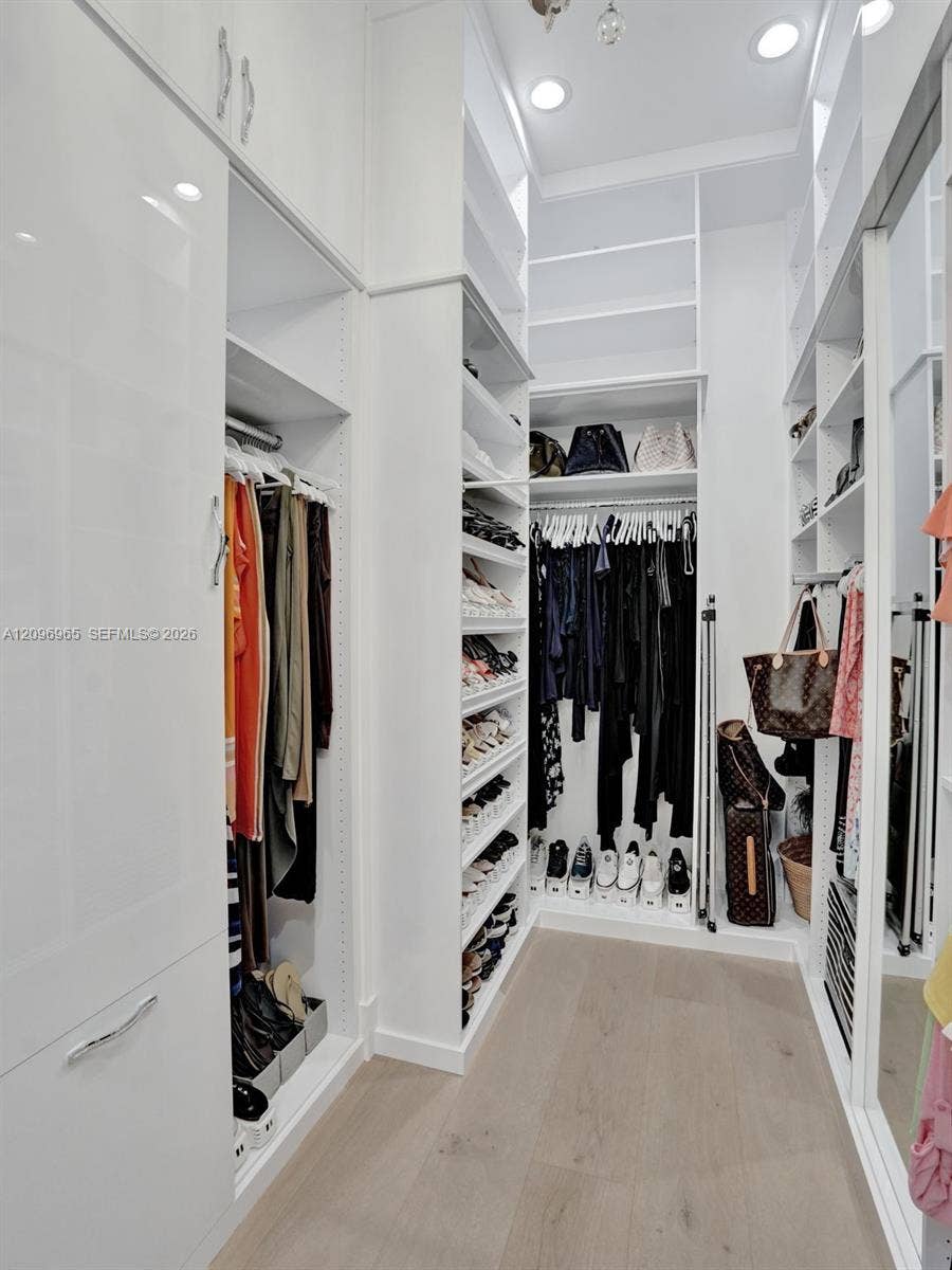 10157 SE Sandpine Lane, Hobe Sound, FL 33455 Custom built-in closet organization featuring high-gloss cabinetry, floor-to-ceiling shelving, multiple hanging rods, and integrated recessed lighting over wood-finish flooring