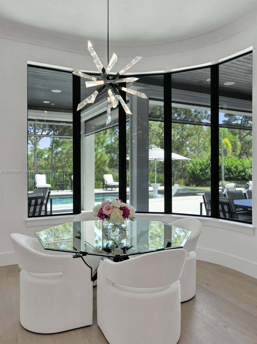 10157 SE Sandpine Lane, Hobe Sound, FL 33455 Curved bay window with black-framed glass panes, wood-finish flooring, and a multi-point geometric pendant light fixture