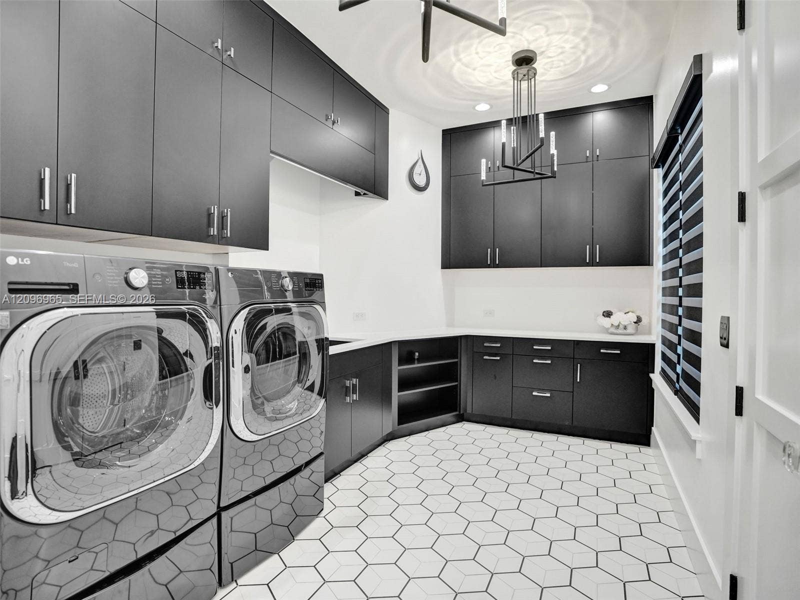 10157 SE Sandpine Lane, Hobe Sound, FL 33455 Laundry room featuring floor-to-ceiling matte black cabinetry, contrasting white countertops, geometric hexagonal floor tile, and modern geometric overhead lighting
