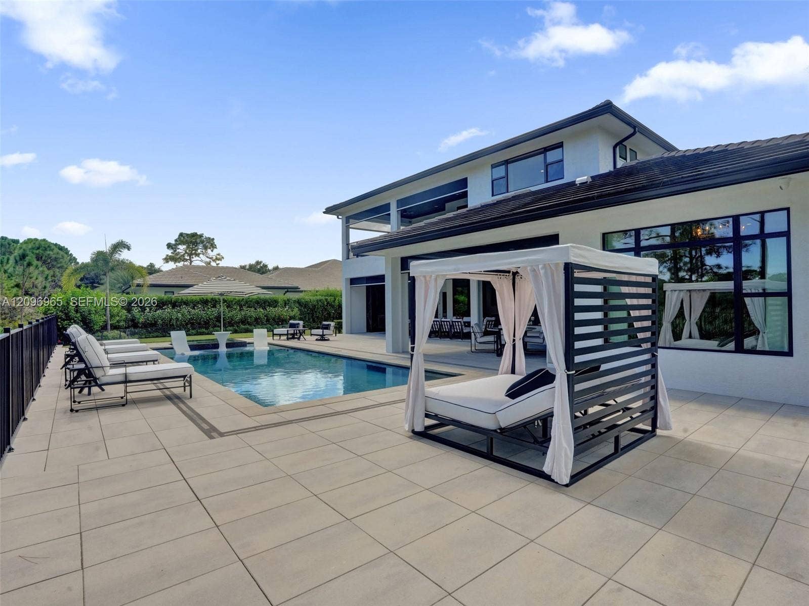 10157 SE Sandpine Lane, Hobe Sound, FL 33455 Rear exterior featuring a spacious tiled patio, an in-ground swimming pool, a covered outdoor area, and large black-framed windows