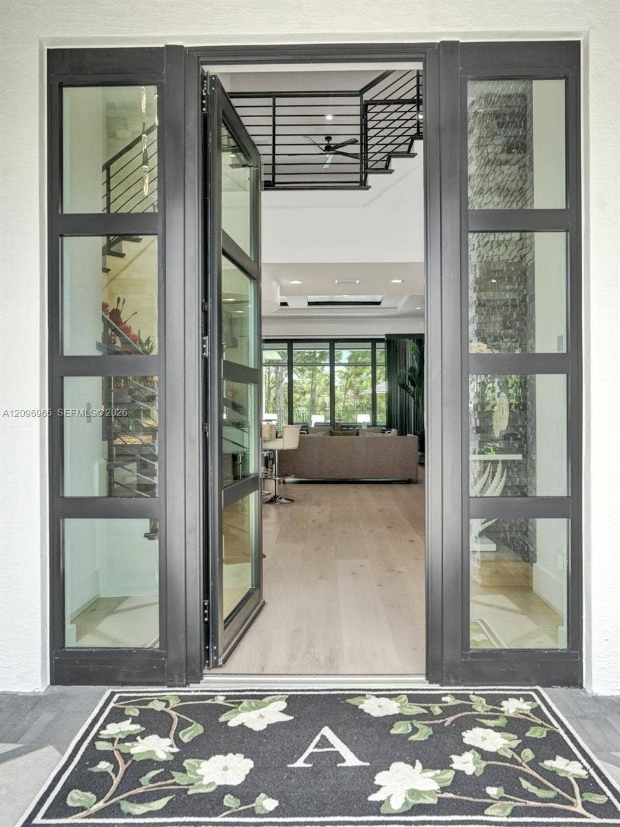 10157 SE Sandpine Lane, Hobe Sound, FL 33455 Modern pivot-style entry door featuring a matte black frame with floor-to-ceiling glass paneling and light-toned wood-finish flooring