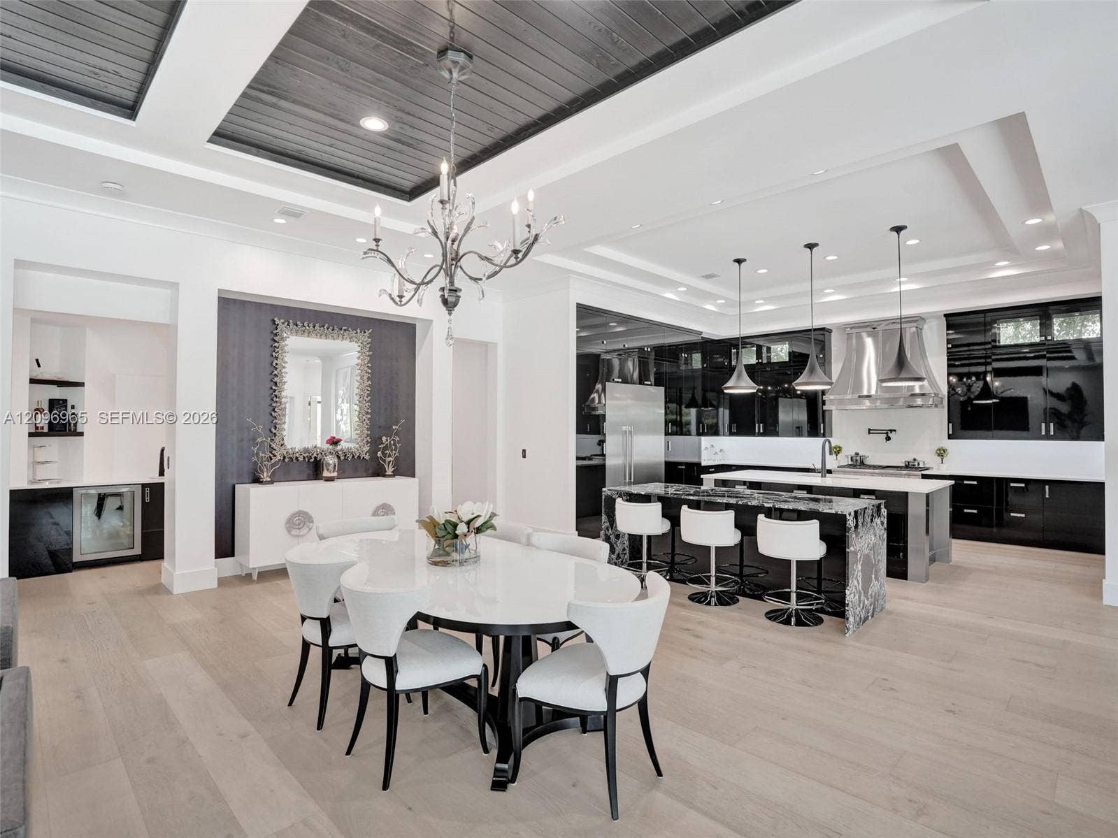 10157 SE Sandpine Lane, Hobe Sound, FL 33455 Open-concept kitchen and dining area featuring wood-finish flooring, a tray ceiling with charcoal-toned wood plank inlay, a custom kitchen island with waterfall-edge stone countertop, and high-gloss cabinetry