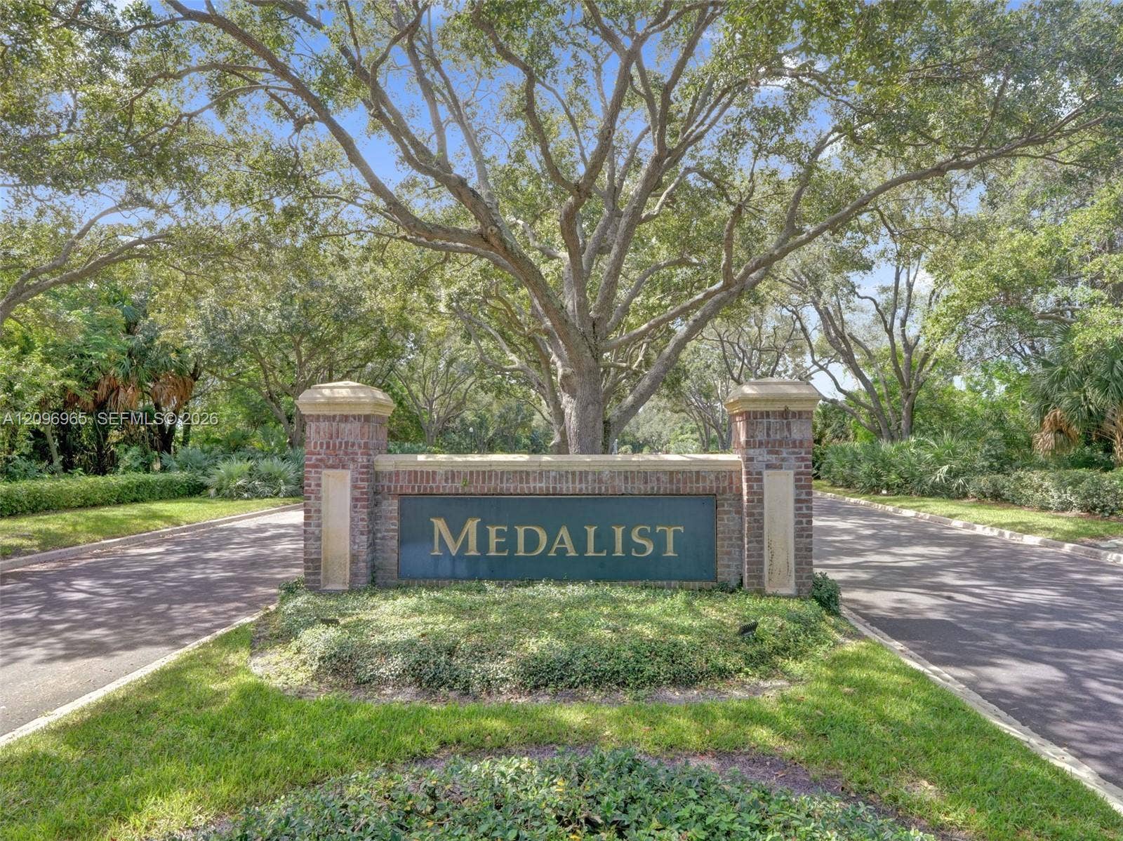 10157 SE Sandpine Lane, Hobe Sound, FL 33455 Brick monument signage featuring stone accents, surrounded by mature trees, landscaping, and paved roadway access