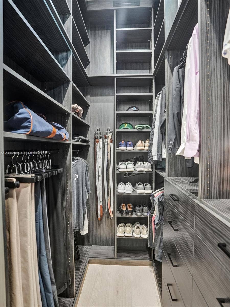 10157 SE Sandpine Lane, Hobe Sound, FL 33455 Walk-in closet featuring dark wood-grain cabinetry, floor-to-ceiling adjustable shelving, integrated hanging rods, built-in dresser drawers with matte black hardware, and wood-finish flooring
