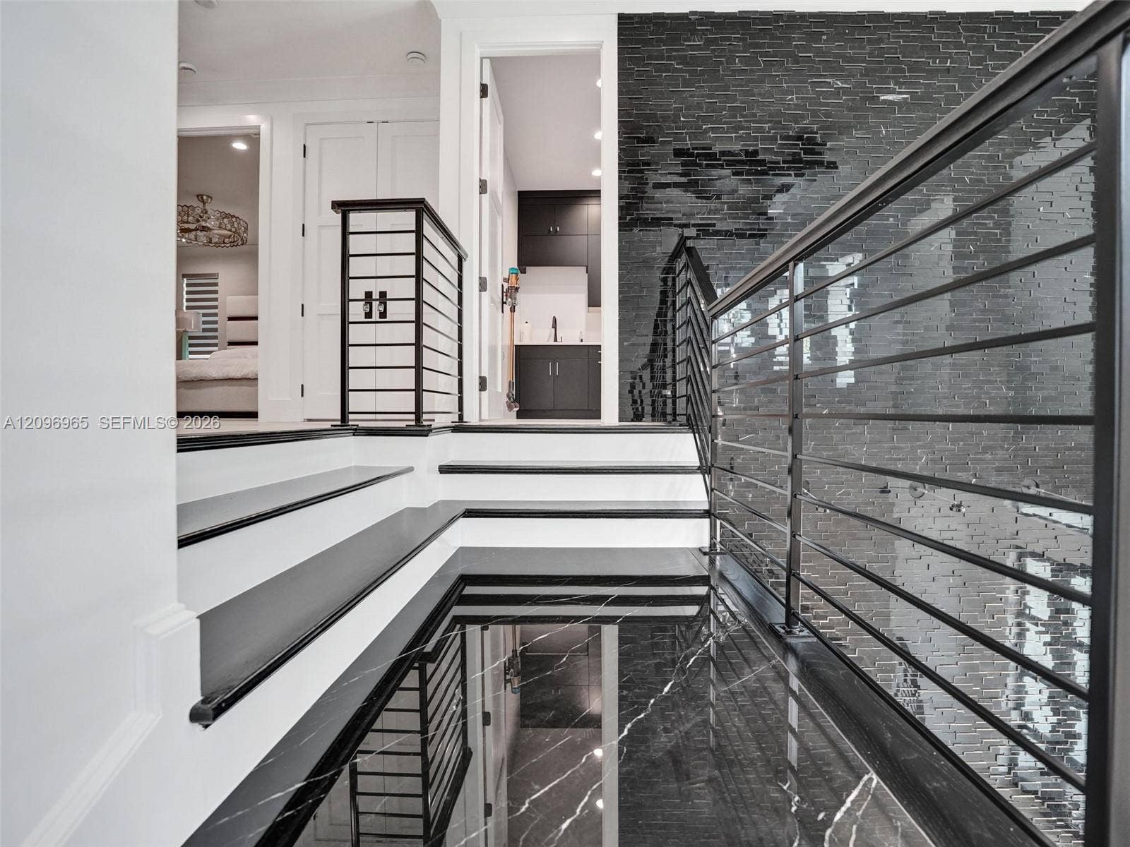 10157 SE Sandpine Lane, Hobe Sound, FL 33455 Staircase featuring dark stone treads, a metal horizontal-bar railing, and a textured black brick accent wall