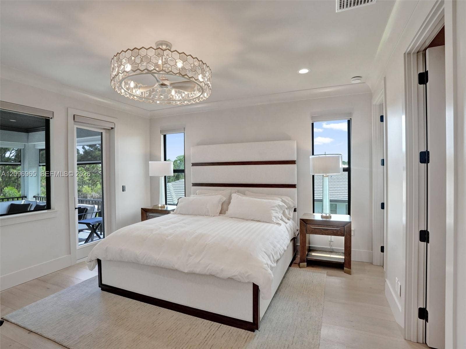 10157 SE Sandpine Lane, Hobe Sound, FL 33455 Spacious room featuring light-toned wood-finish flooring, crown molding, a decorative multi-light ceiling fixture, and black-framed windows and exterior door