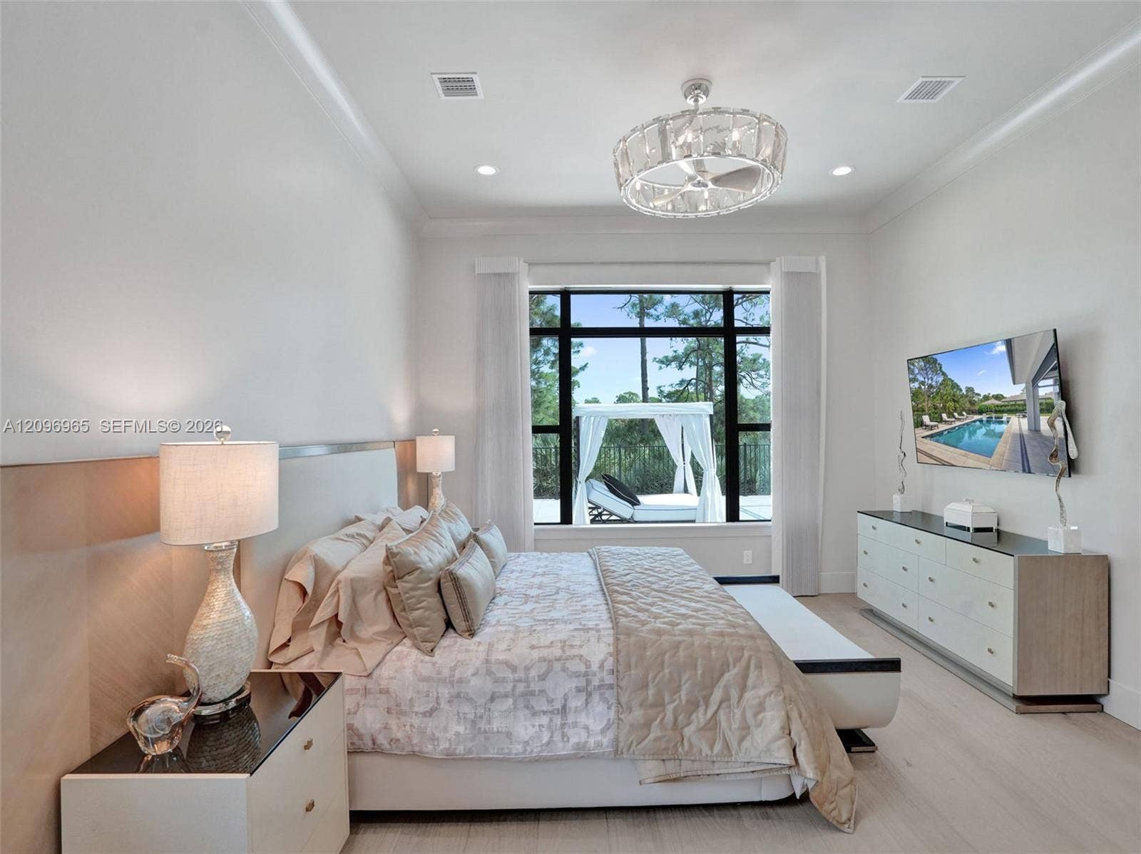 10157 SE Sandpine Lane, Hobe Sound, FL 33455 Neutral-toned bedroom featuring crown molding, wood-finish flooring, a decorative crystal-style ceiling fan, and large floor-to-ceiling windows with black framing