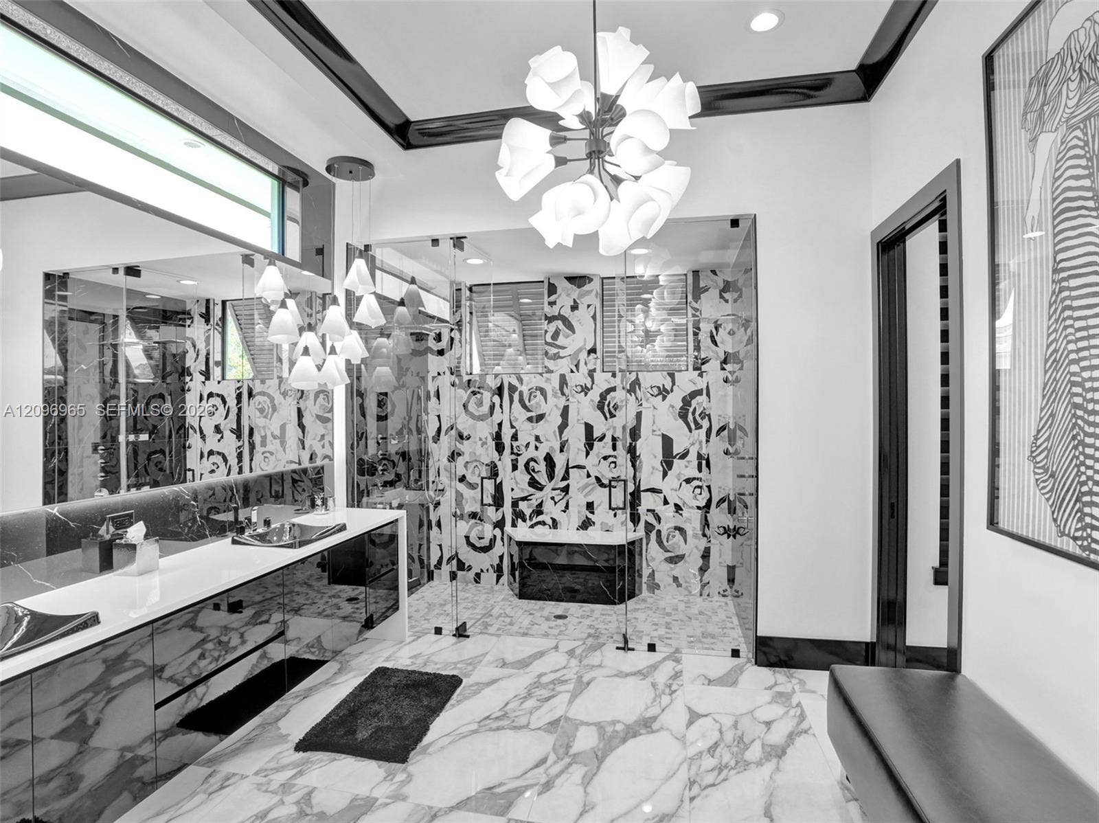 10157 SE Sandpine Lane, Hobe Sound, FL 33455 Bathroom featuring a custom floating vanity with integrated sinks, floor-to-ceiling patterned wall tile, glass-enclosed walk-in shower, large-format stone flooring, and tiered multi-light chandelier