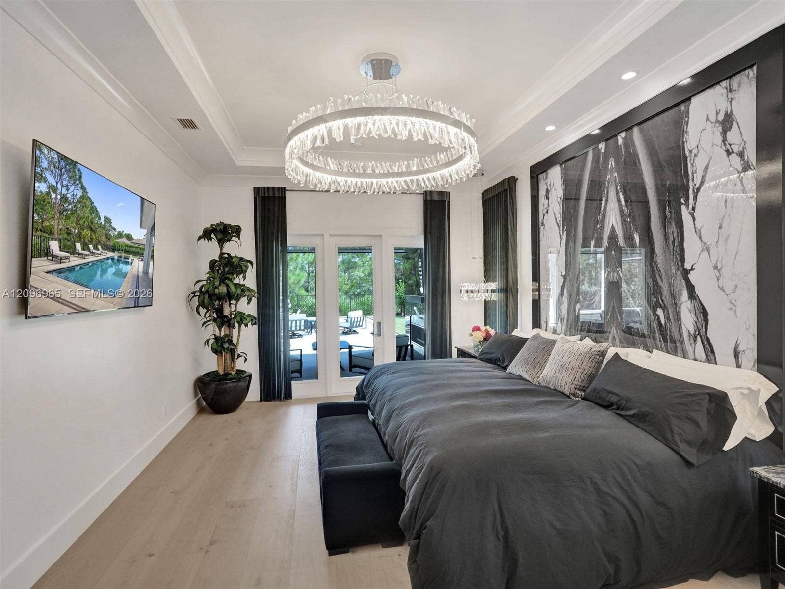 10157 SE Sandpine Lane, Hobe Sound, FL 33455 Tray ceiling featuring a large circular crystal chandelier, light-toned wood-finish flooring, and a floor-to-ceiling stone-clad wall accent