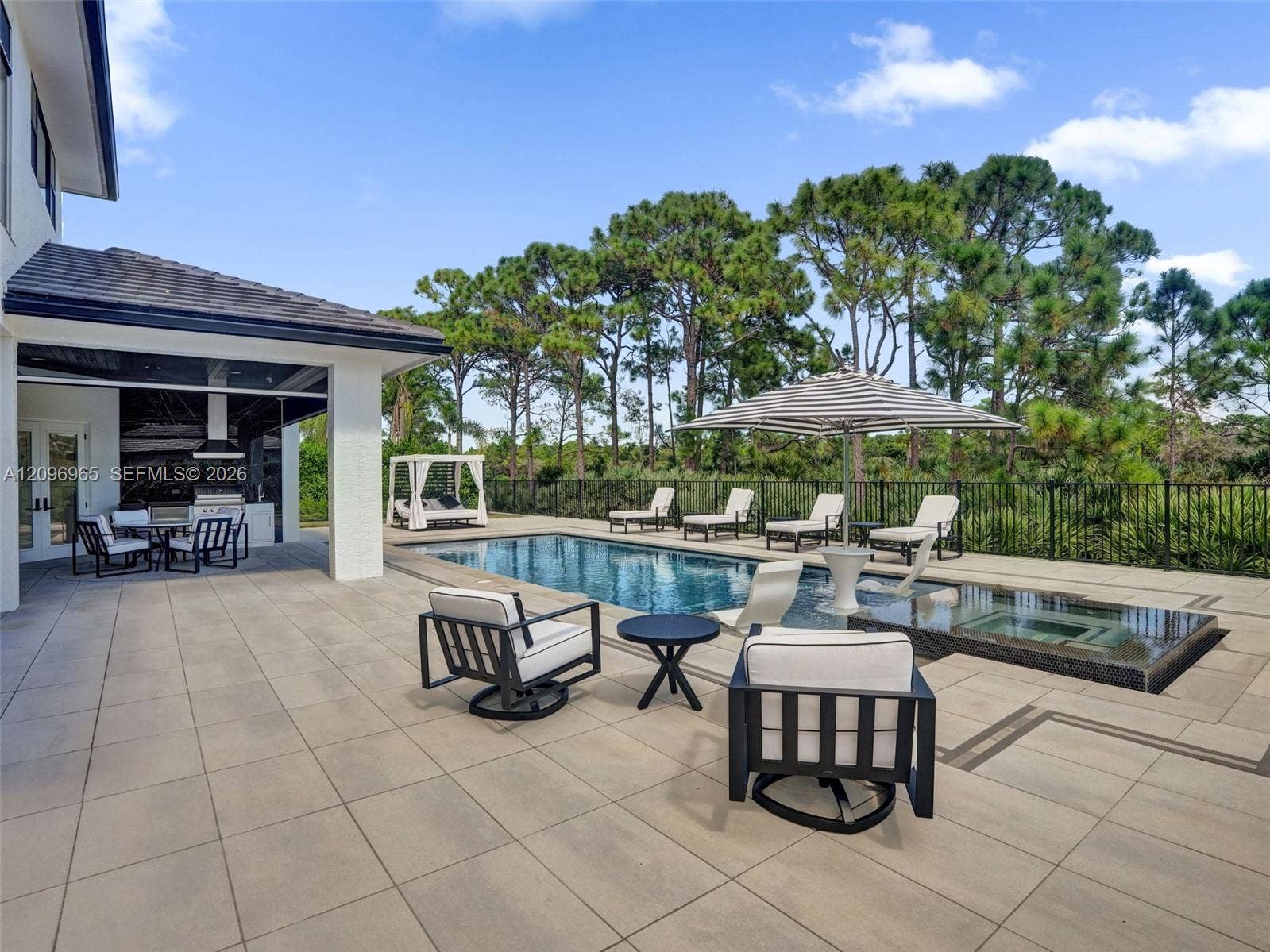 10157 SE Sandpine Lane, Hobe Sound, FL 33455 Expansive paved patio with a covered outdoor kitchen, rectangular swimming pool, raised spa, and black metal perimeter fencing
