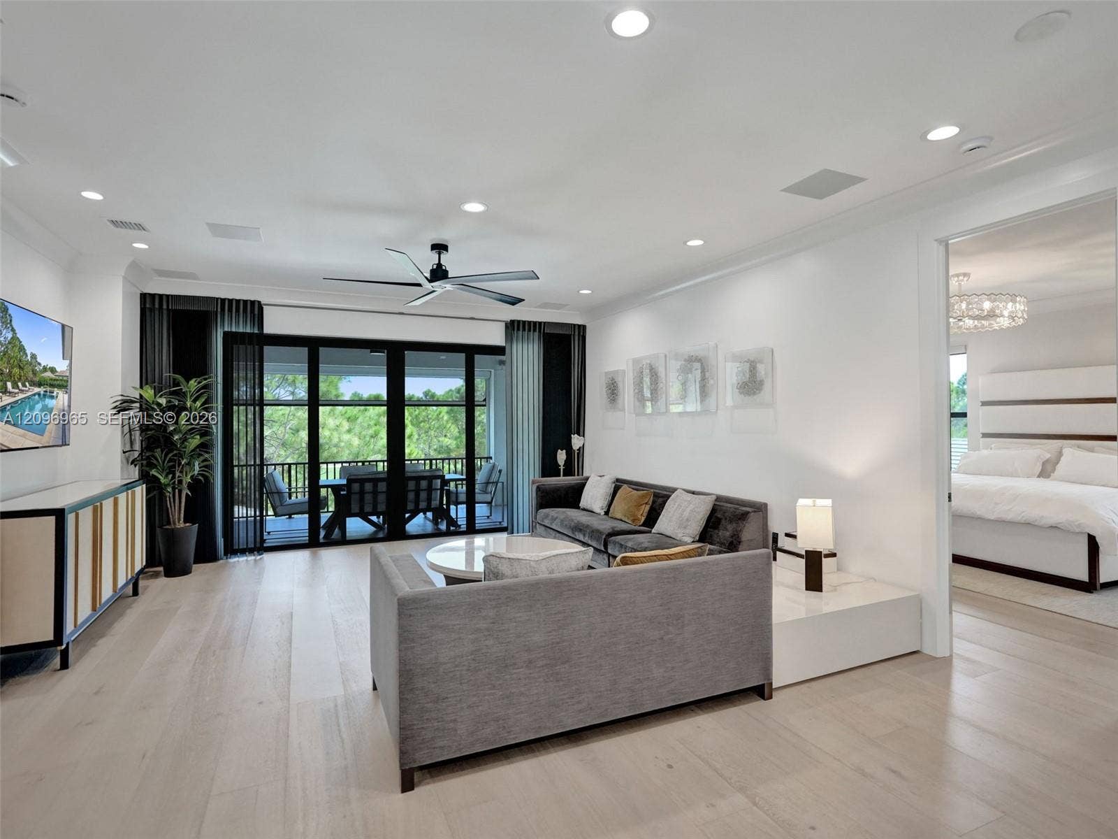 10157 SE Sandpine Lane, Hobe Sound, FL 33455 Open-concept interior featuring light wood-finish flooring, recessed lighting, a modern ceiling fan, and black-framed glass sliding doors opening to a covered balcony
