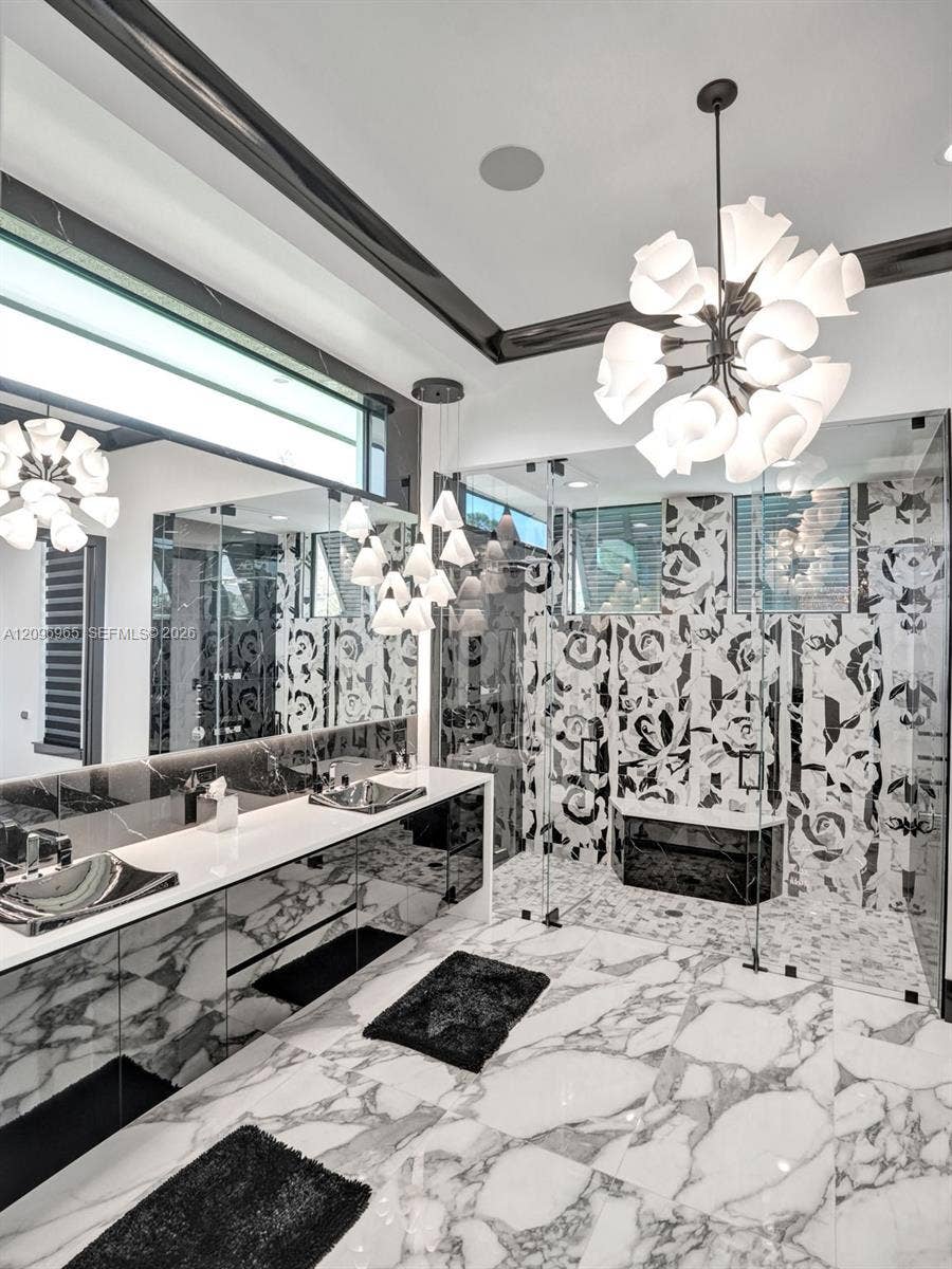 10157 SE Sandpine Lane, Hobe Sound, FL 33455 Dual vanity featuring vessel sinks, custom cabinetry, patterned stone wall detailing, glass-enclosed shower, and statement pendant lighting