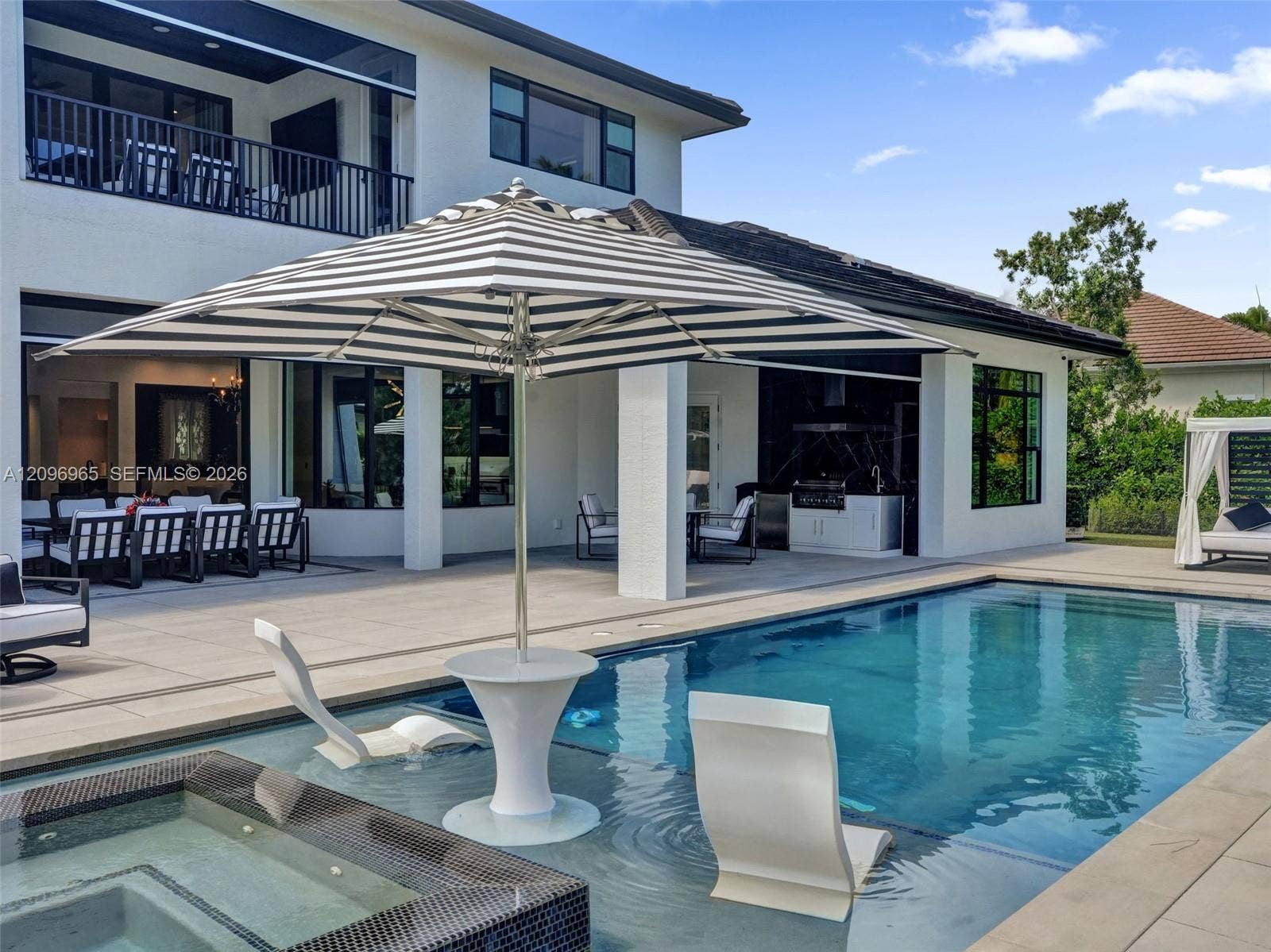10157 SE Sandpine Lane, Hobe Sound, FL 33455 Swimming pool featuring a sun shelf with a built-in table, integrated spa, covered patio, and outdoor kitchen