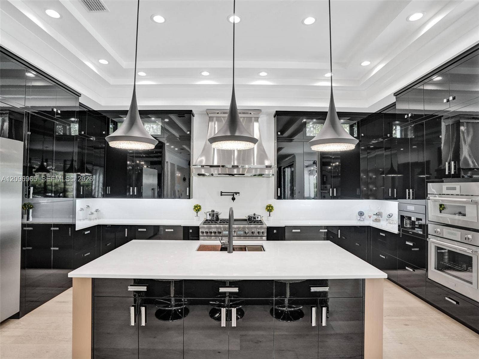 10157 SE Sandpine Lane, Hobe Sound, FL 33455 Kitchen featuring high-gloss black cabinetry, center island with stone countertop, stainless steel professional-grade range with coordinating hood, triple pendant lighting, and recessed ceiling illumination