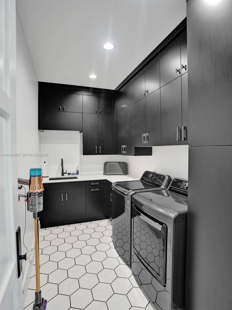 10157 SE Sandpine Lane, Hobe Sound, FL 33455 Laundry area featuring full-height matte black cabinetry, contrasting white countertops, an integrated basin with a matte black faucet, and geometric hexagonal floor tile