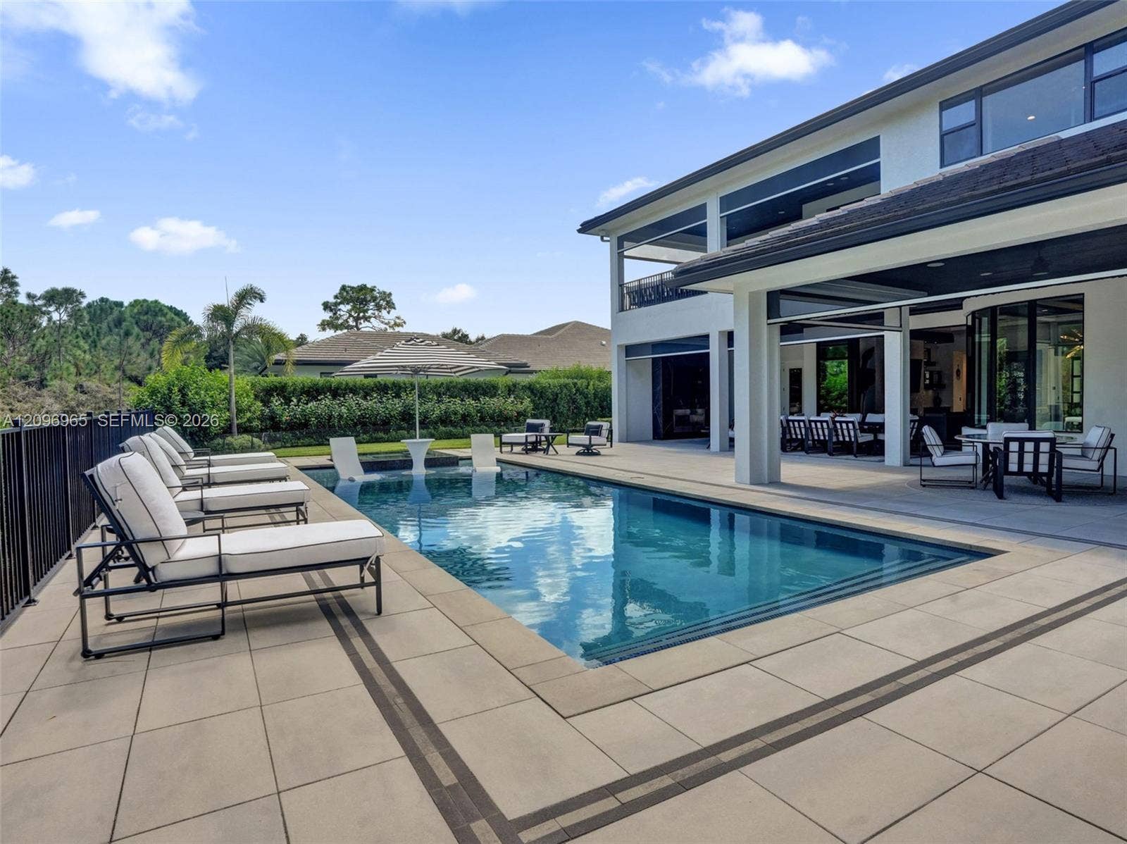 10157 SE Sandpine Lane, Hobe Sound, FL 33455 Outdoor living area featuring a custom swimming pool with a built-in sun shelf, expansive stone-paver decking, and a covered lanai