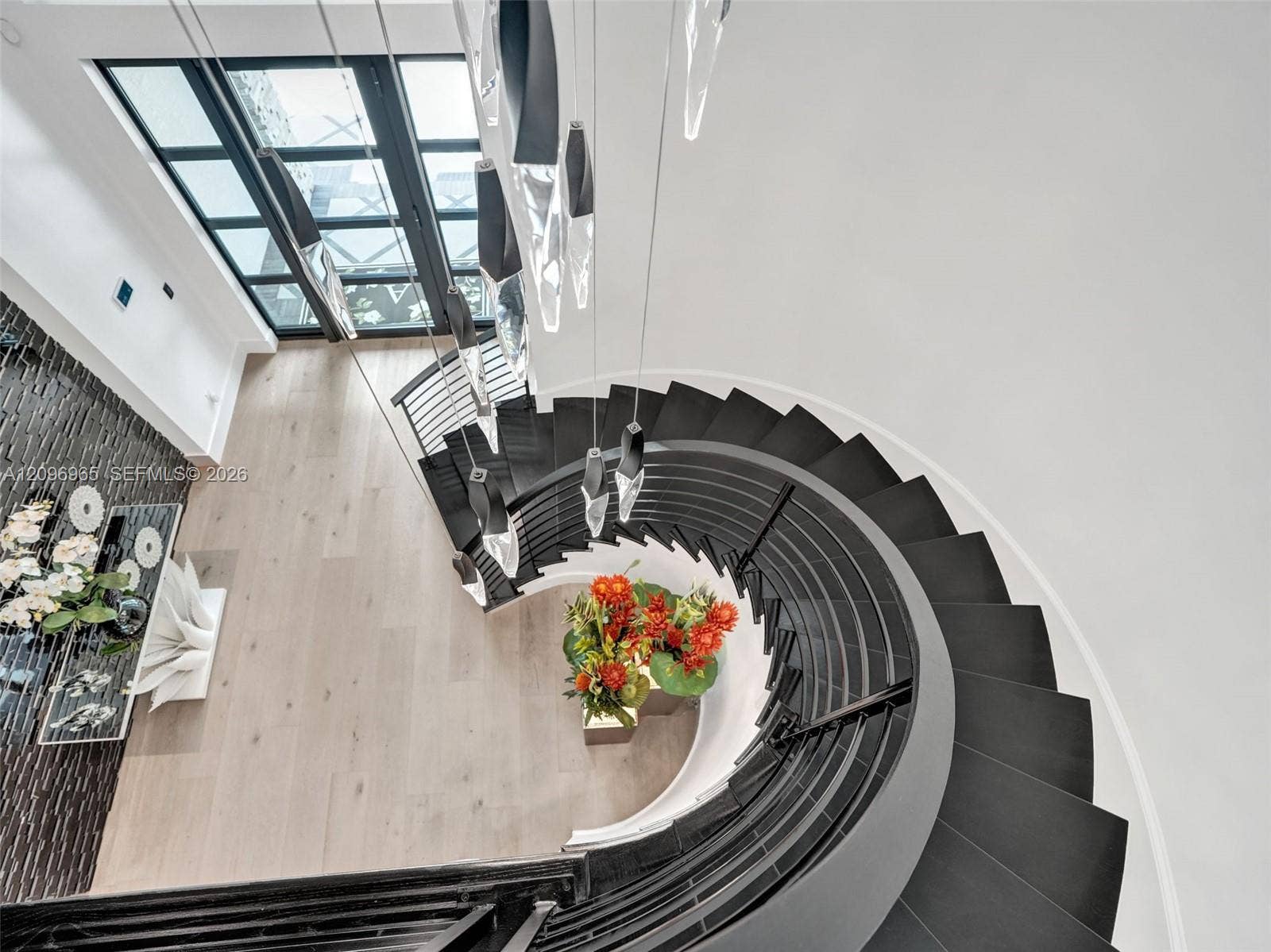 10157 SE Sandpine Lane, Hobe Sound, FL 33455 Curved staircase featuring dark treads, black metal railing, floor-to-ceiling glass-paneled door, modern multi-pendant light fixture, and wood-finish flooring