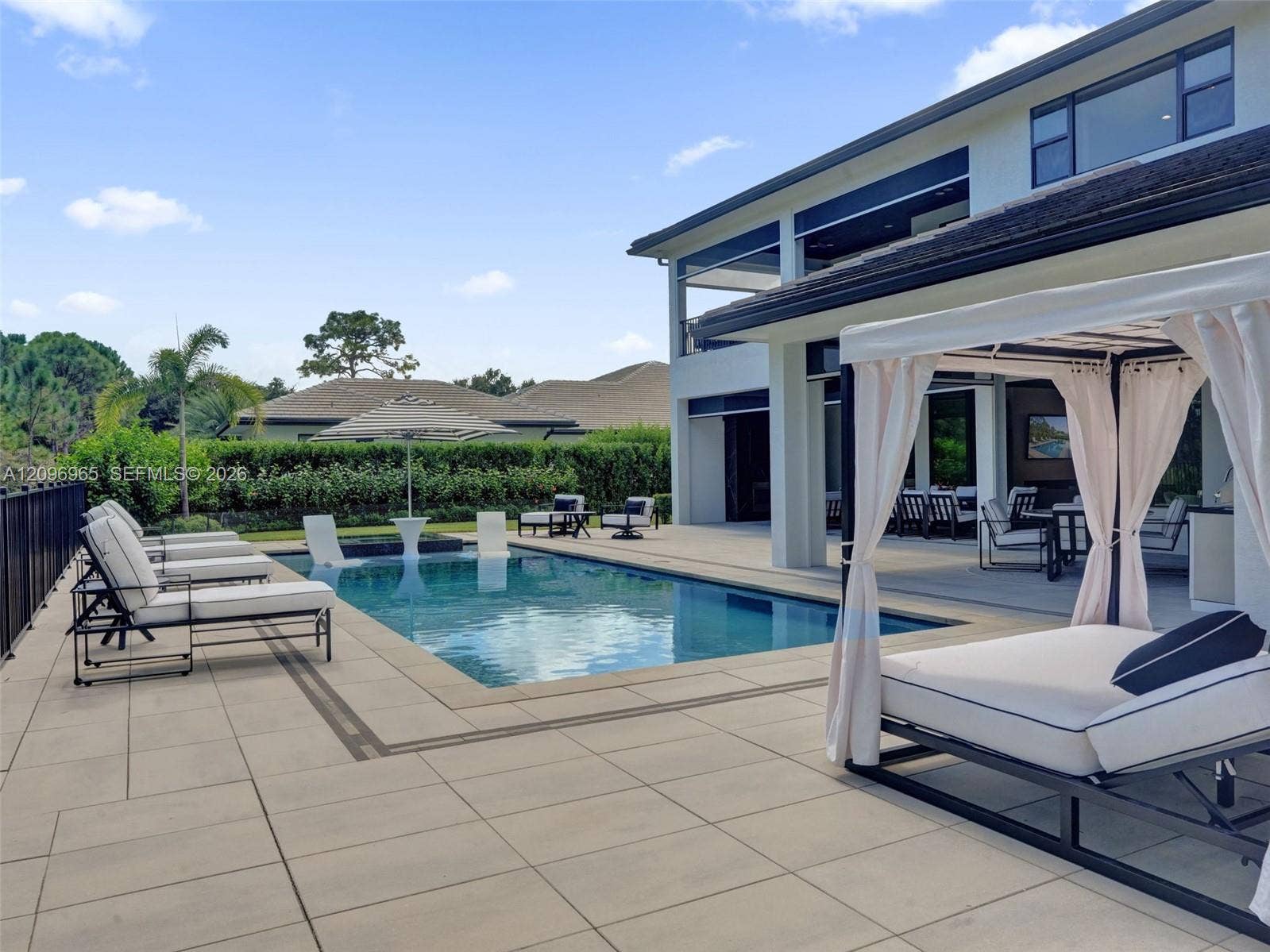 10157 SE Sandpine Lane, Hobe Sound, FL 33455 Backyard featuring a rectangular swimming pool, integrated shallow sun shelf, expansive stone-finish decking, and a covered lanai