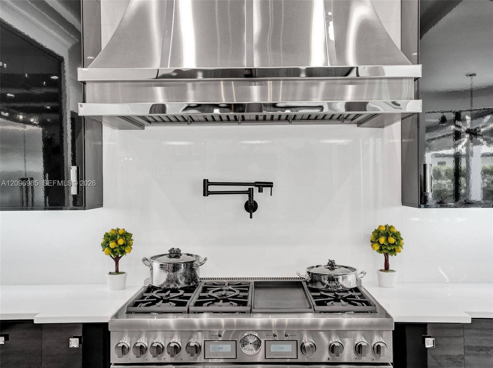 10157 SE Sandpine Lane, Hobe Sound, FL 33455 Stainless steel professional-grade range with integrated griddle, wall-mounted matte black pot filler, oversized stainless steel range hood, and solid-surface backsplash