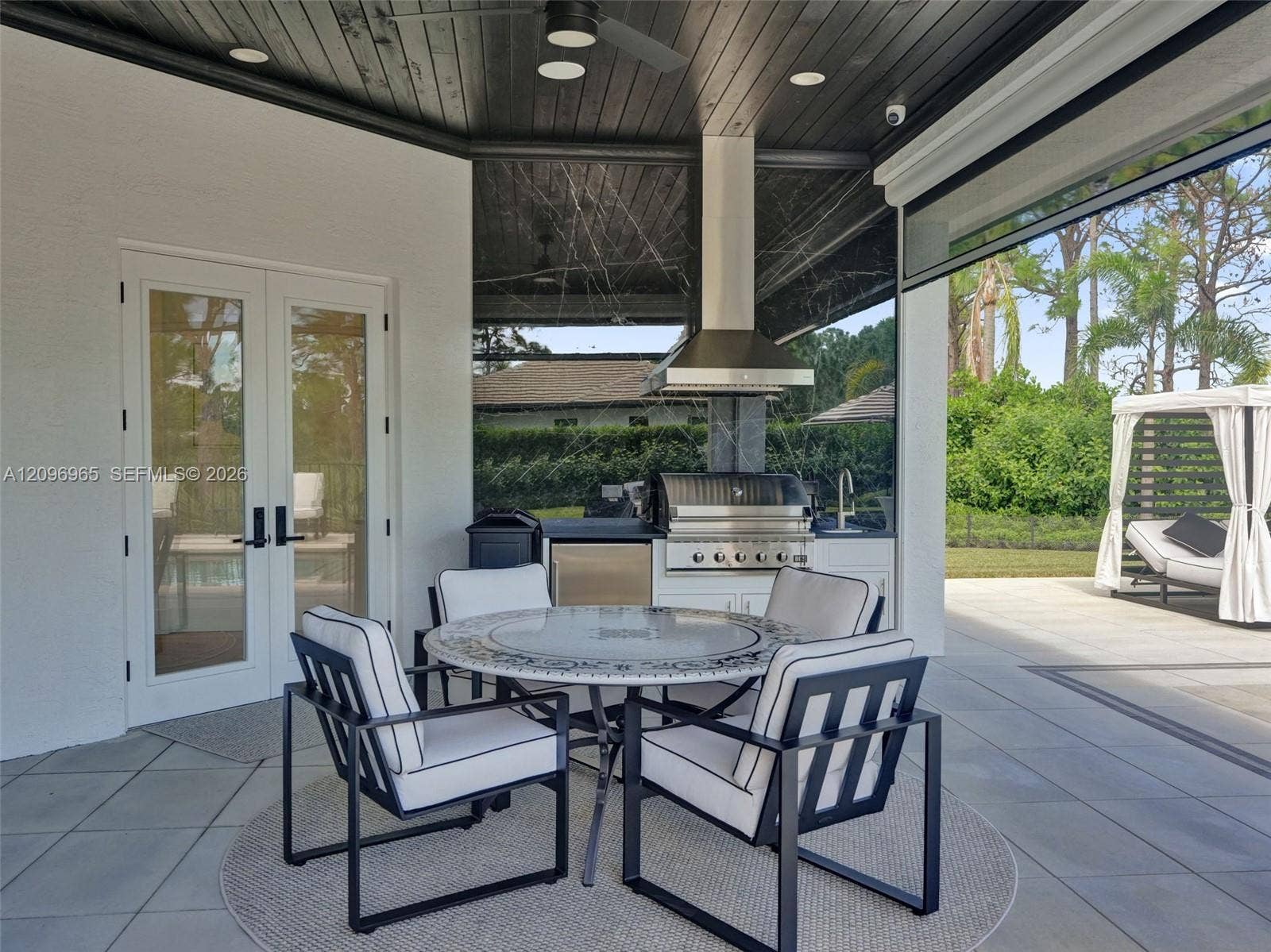 10157 SE Sandpine Lane, Hobe Sound, FL 33455 Covered outdoor kitchen featuring a stainless steel grill, stainless steel under-counter refrigerator, sink, and dark wood-finish tongue-and-groove ceiling with recessed lighting
