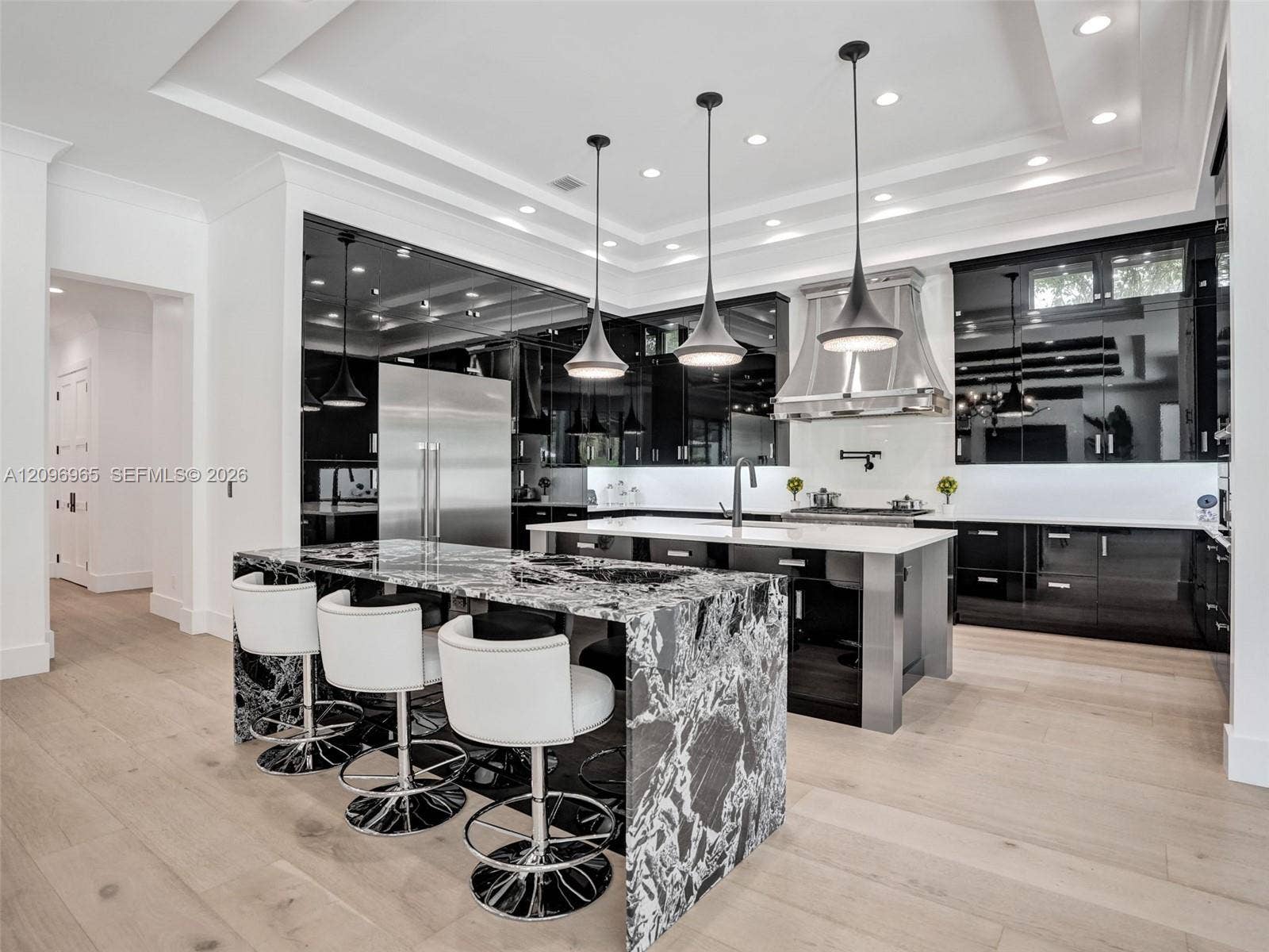 10157 SE Sandpine Lane, Hobe Sound, FL 33455 Kitchen featuring high-gloss black cabinetry, waterfall-edge stone island, stainless steel range hood, recessed tray ceiling, and wood-finish flooring