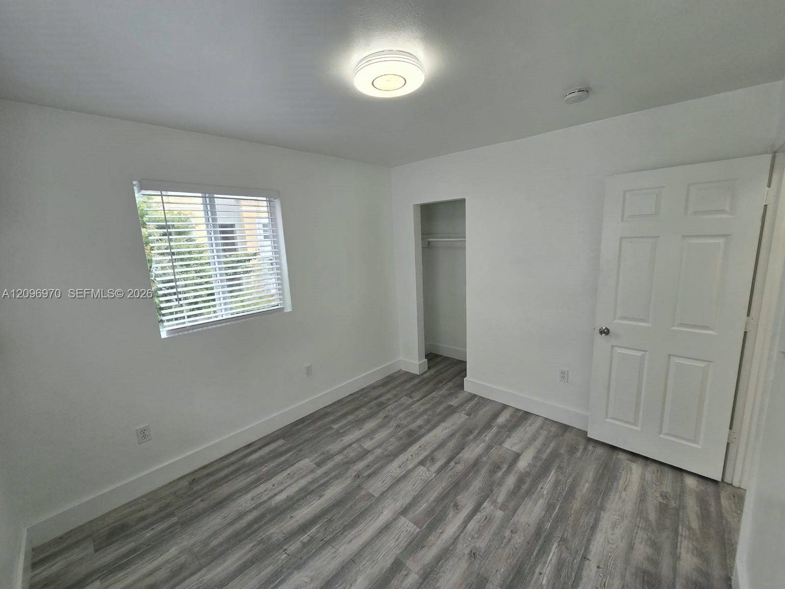 535 NW 7th Street, #12, Miami, Miami, FL 33136 Interior space featuring wood-finish flooring, a recessed closet with built-in shelving, a flush-mount overhead light fixture, and a window with horizontal blinds