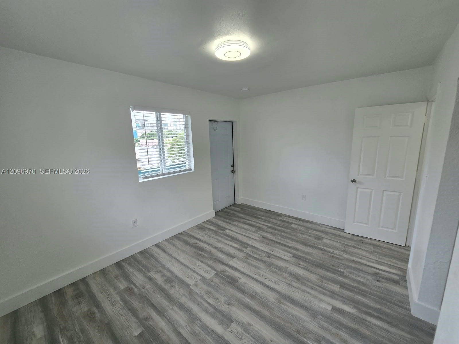 535 NW 7th Street, #12, Miami, Miami, FL 33136 Interior space featuring neutral wall paint, wood-finish flooring, a flush-mount circular ceiling light, a multi-pane window, and a six-panel door