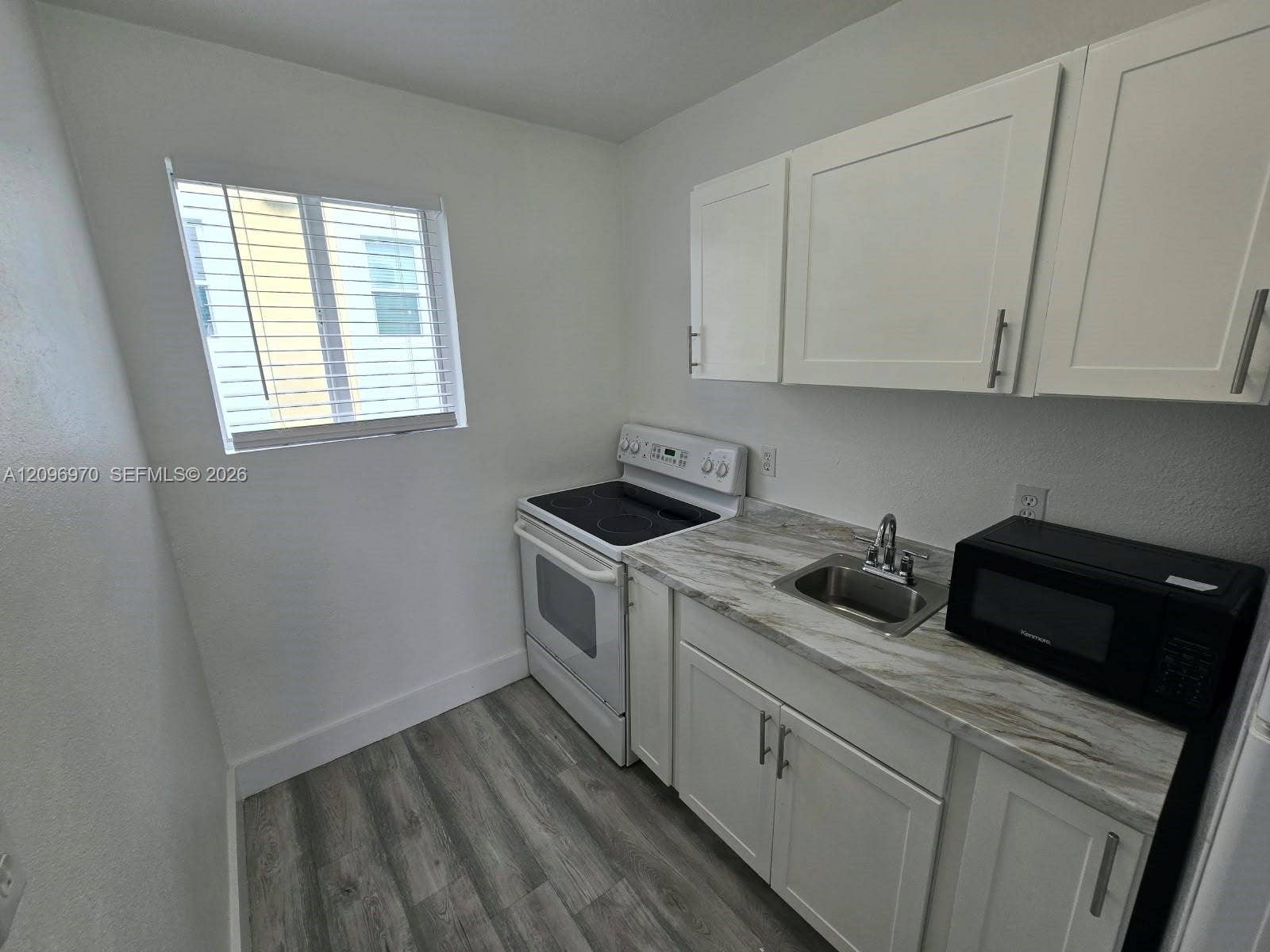 535 NW 7th Street, #12, Miami, Miami, FL 33136 Kitchen featuring white shaker-style cabinetry, stone-patterned laminate countertops, stainless steel sink with pull-out faucet, and wood-finish flooring